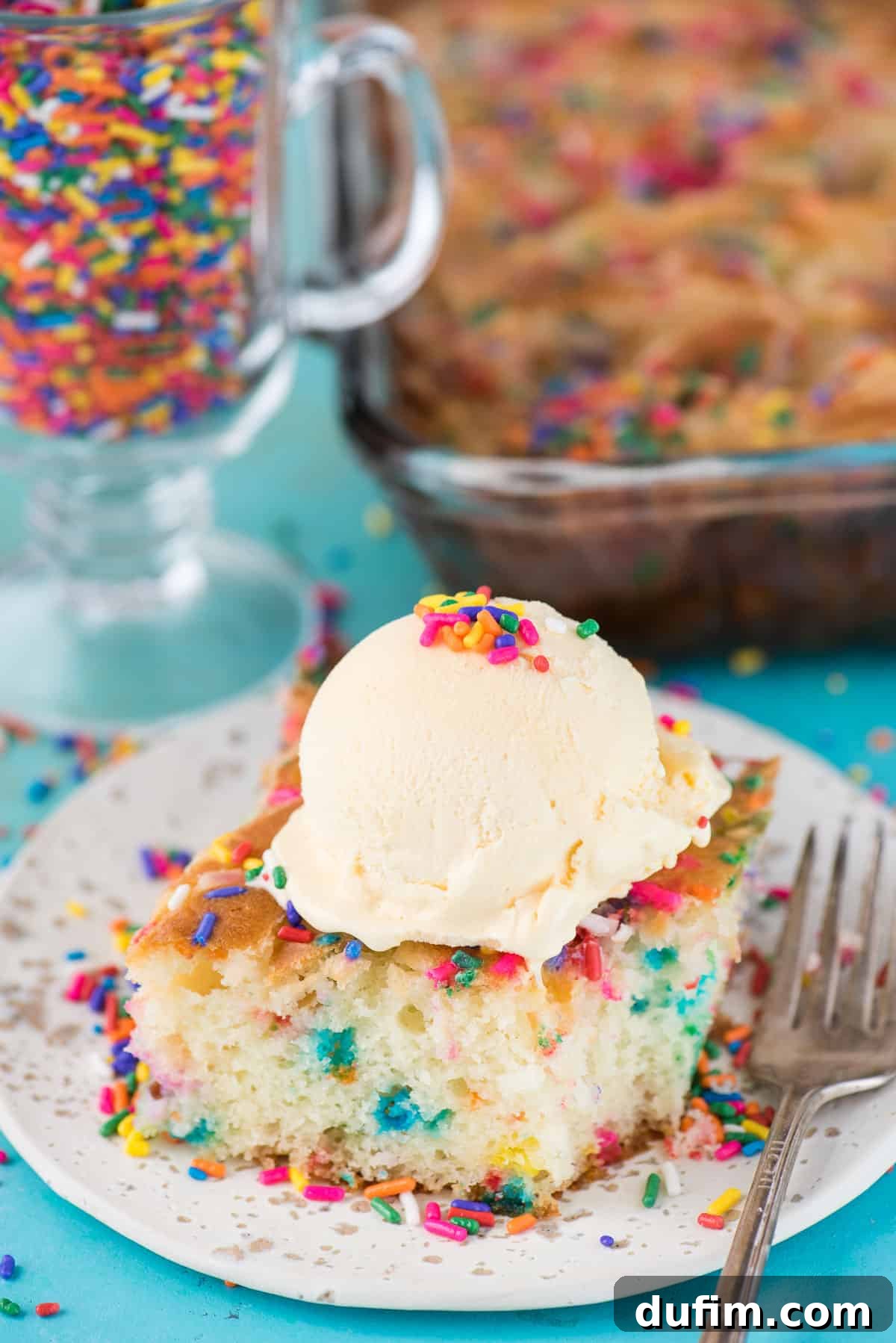 A vibrant slice of Funfetti Earthquake Cake, rich with sprinkles and a creamy swirl, served with a scoop of vanilla ice cream on a white plate, set against a cheerful blue background.