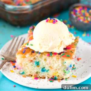 A delicious slice of Funfetti Earthquake Cake topped with vanilla ice cream and colorful sprinkles sits on a white plate, ready to be enjoyed.
