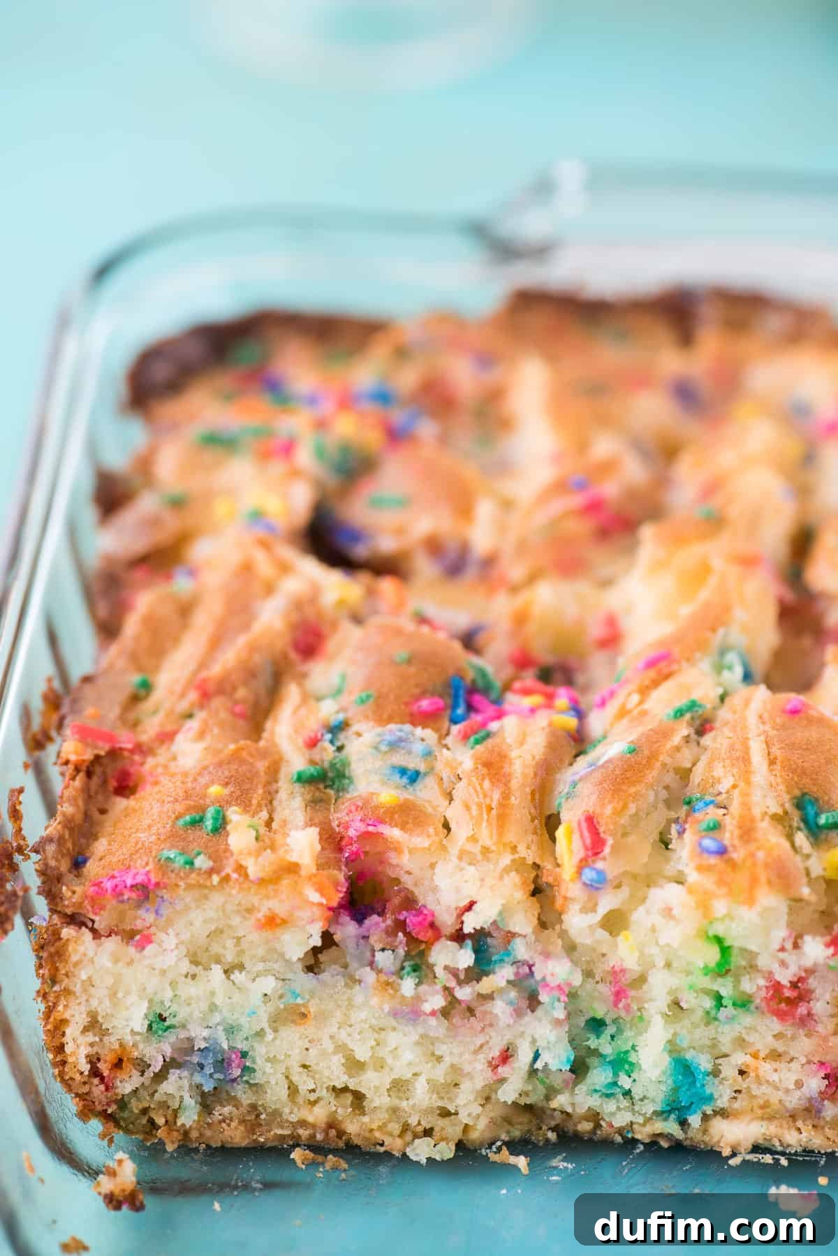 A baking dish containing an unbaked Funfetti Earthquake Cake, showing the swirled cream cheese frosting on top of the colorful batter, ready for the oven.
