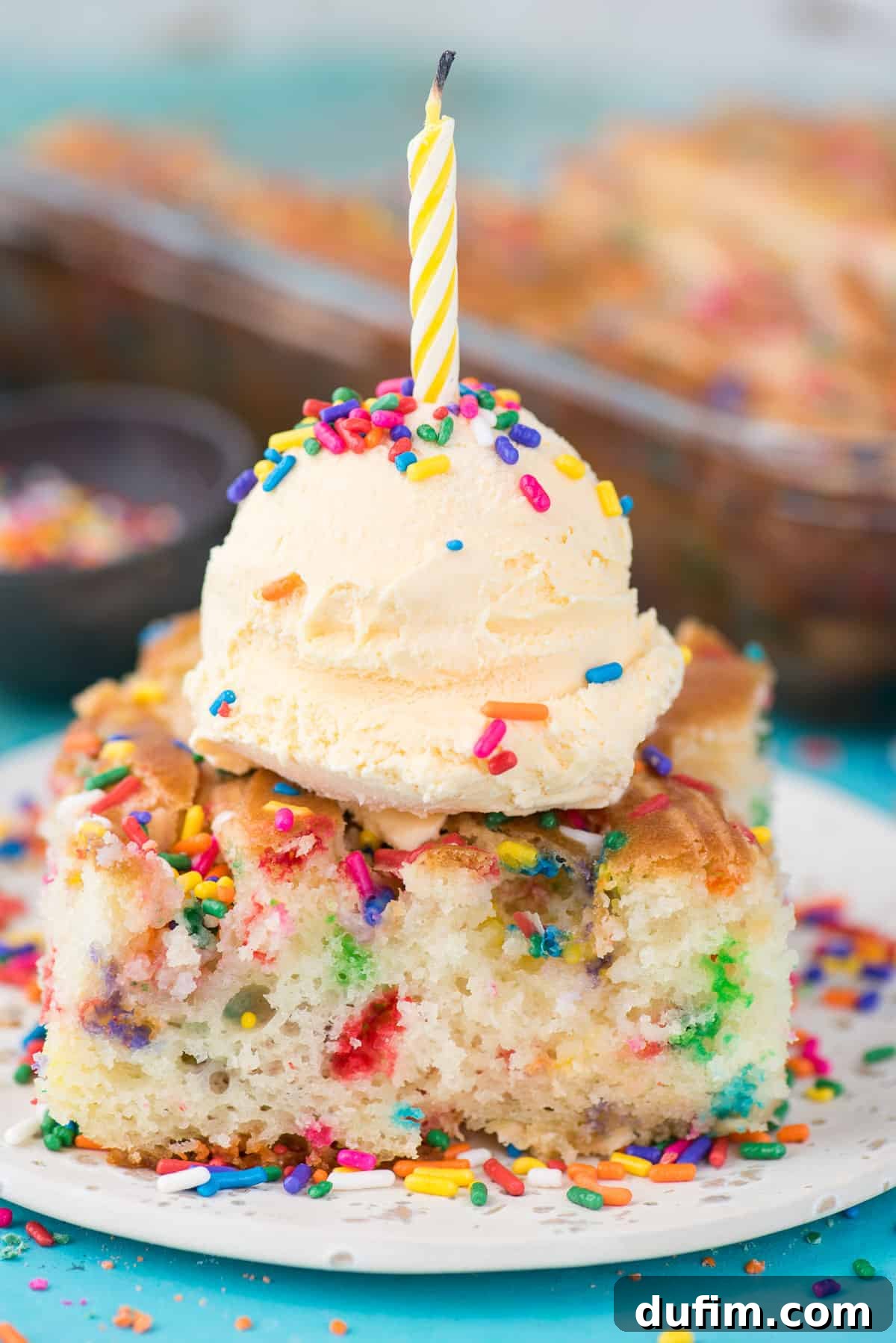 A close-up of a delicious slice of Funfetti Earthquake Cake, revealing the moist crumb, embedded sprinkles, and creamy streaks, served on a white plate with ice cream.