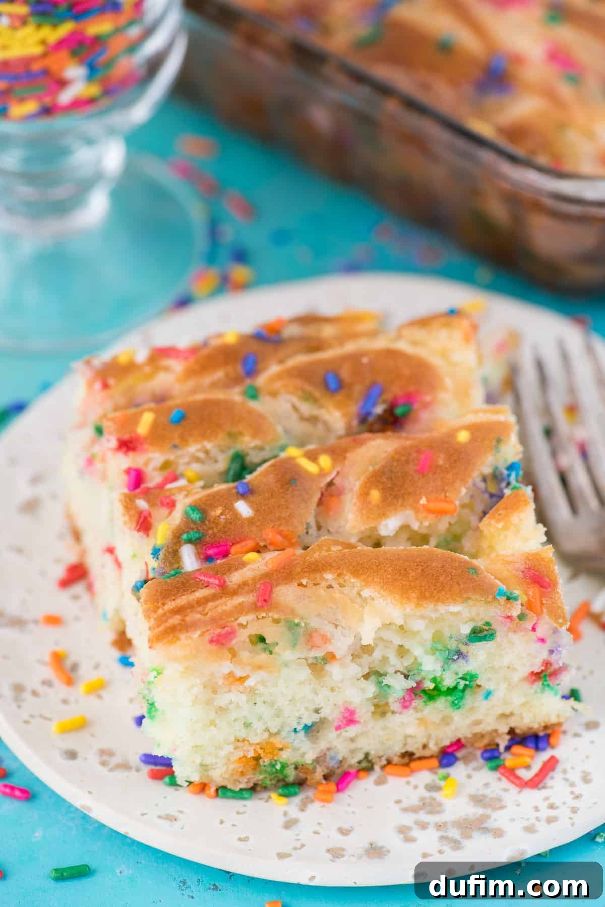 A perfectly portioned slice of Funfetti Earthquake Cake, showcasing its colorful sprinkles and moist texture, rests on a pristine white plate against a serene blue background.