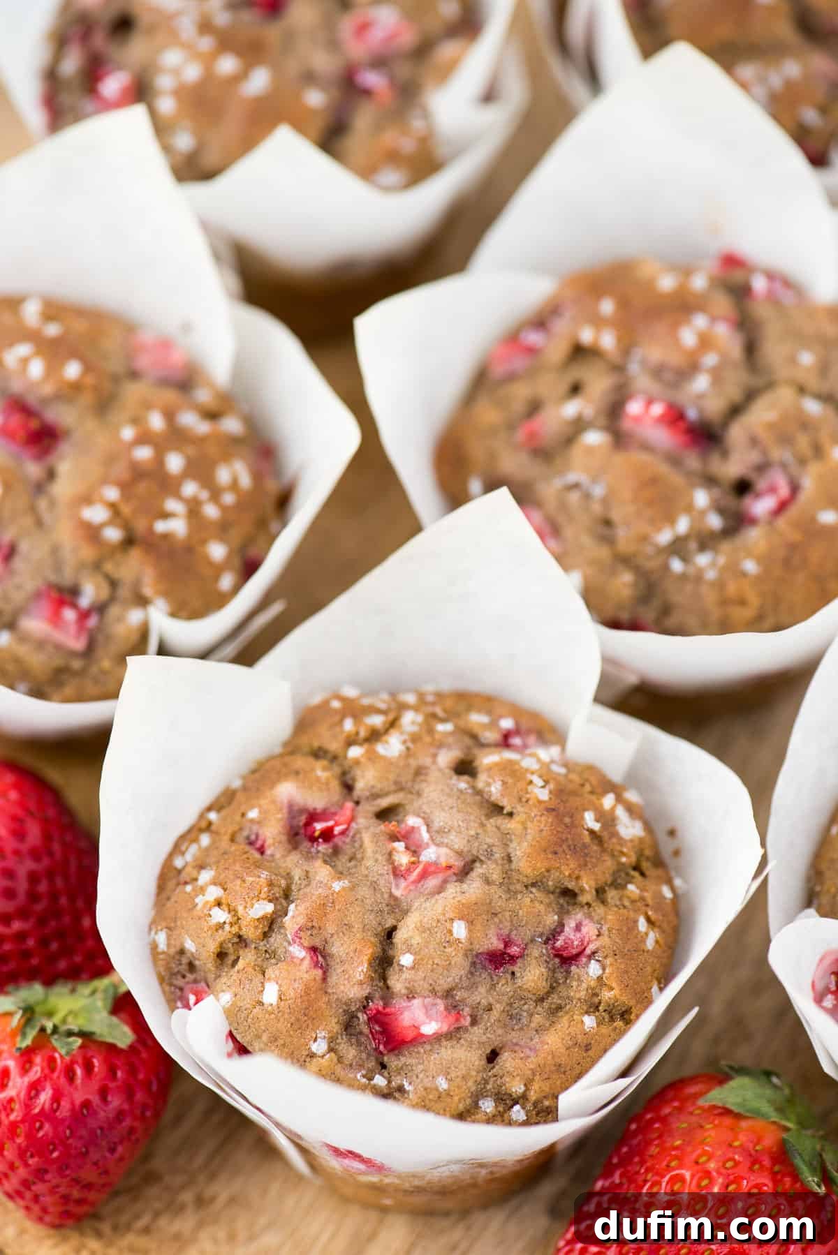 Freshly baked strawberry banana muffins in elegant white parchment paper liners, artfully arranged on a rustic wooden background.