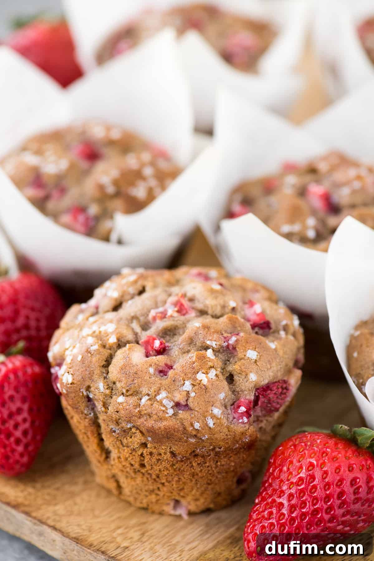 A delightful array of strawberry banana muffins, baked to golden perfection in white parchment paper liners, resting on a textured wooden surface.