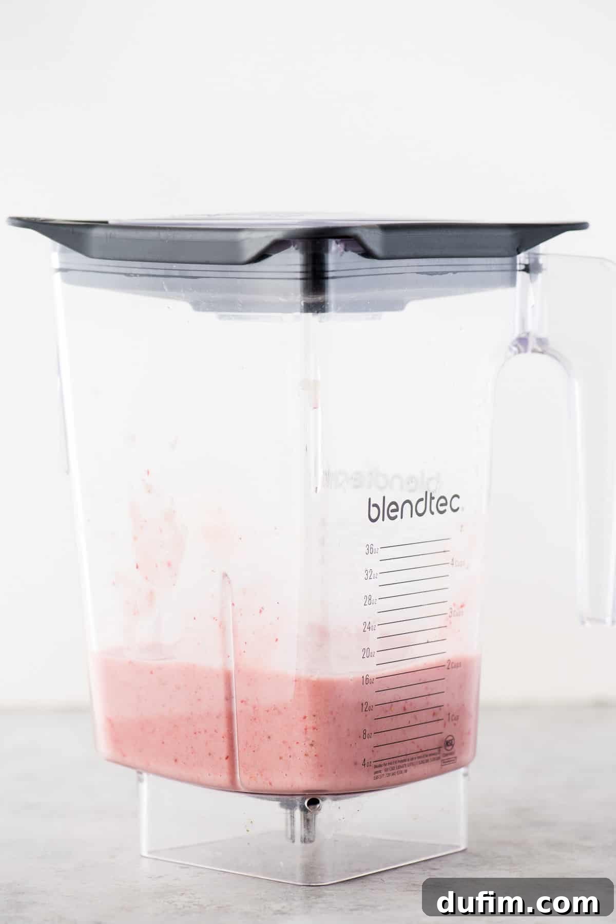 A vibrant, smooth mixture of pureed strawberries and bananas swirling in a blender, forming the flavorful base for these homemade muffins.