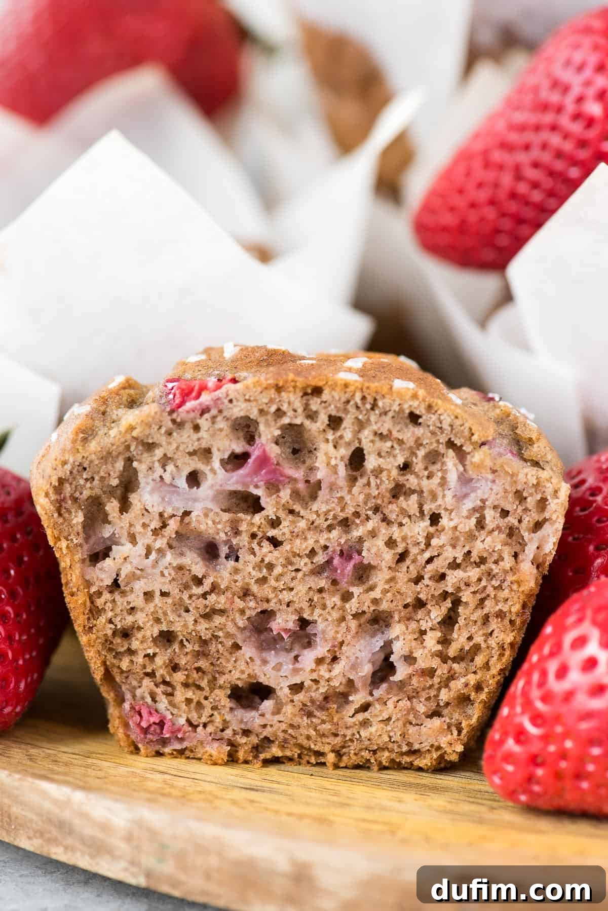 A perfectly baked strawberry banana muffin, neatly sliced in half to reveal its tender, fruit-studded interior, presented on a rustic wooden background.