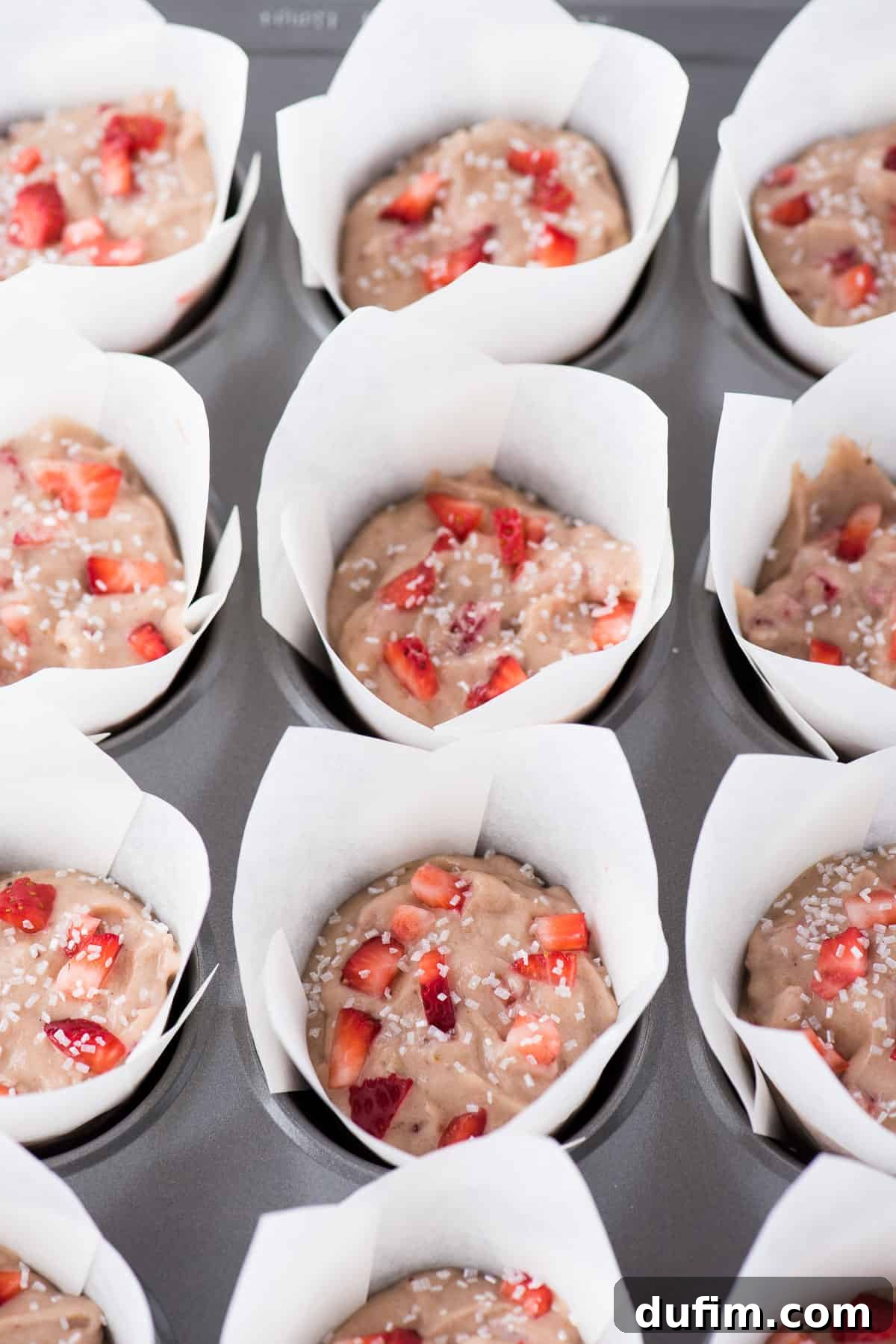 Muffin batter meticulously filled into white parchment paper tulip liners within a muffin pan, poised and ready for its transformation in the oven.