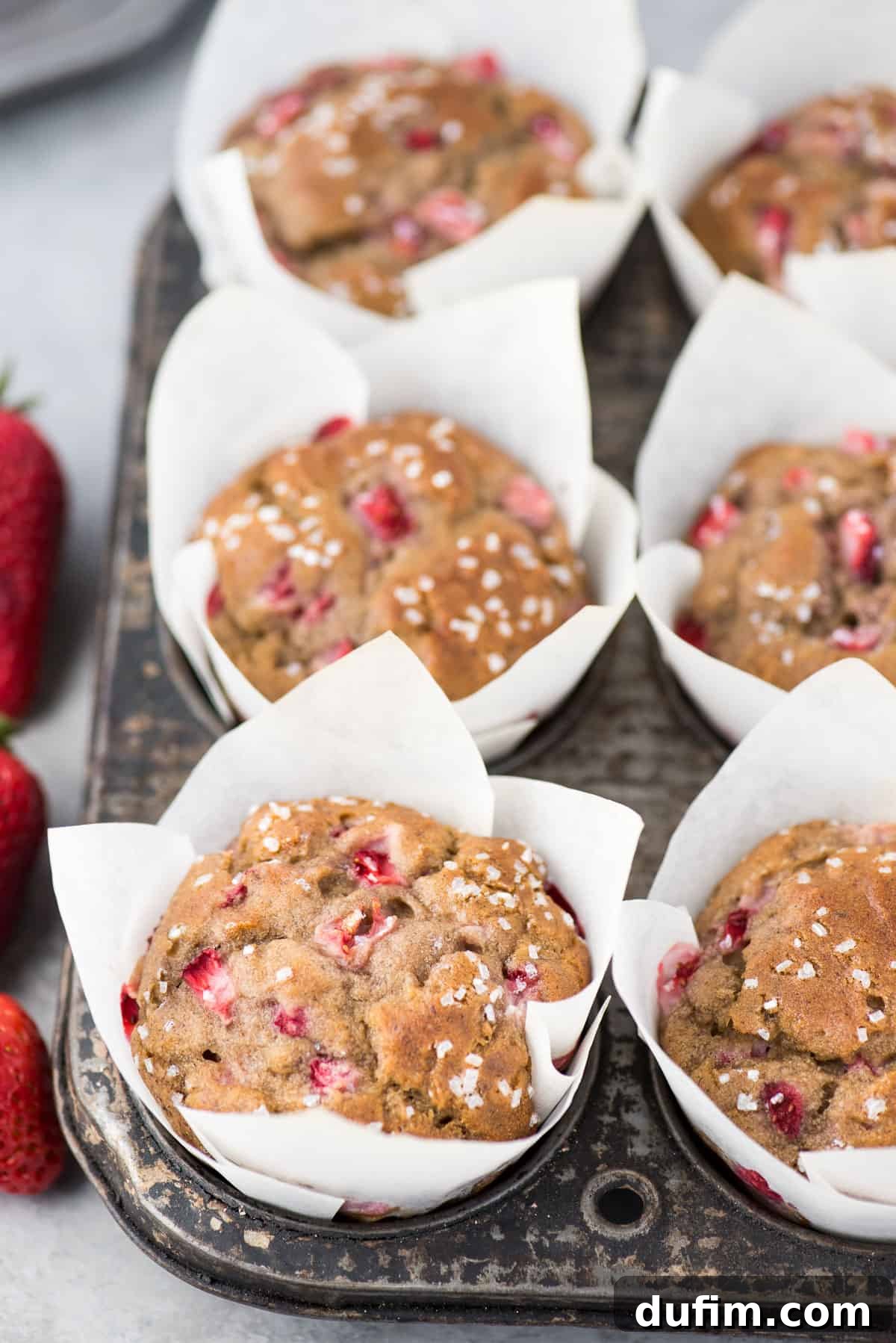 A pristine tray of unbaked strawberry banana muffins, adorned with diced strawberries, nestled in white parchment paper liners, poised for their journey into the oven.