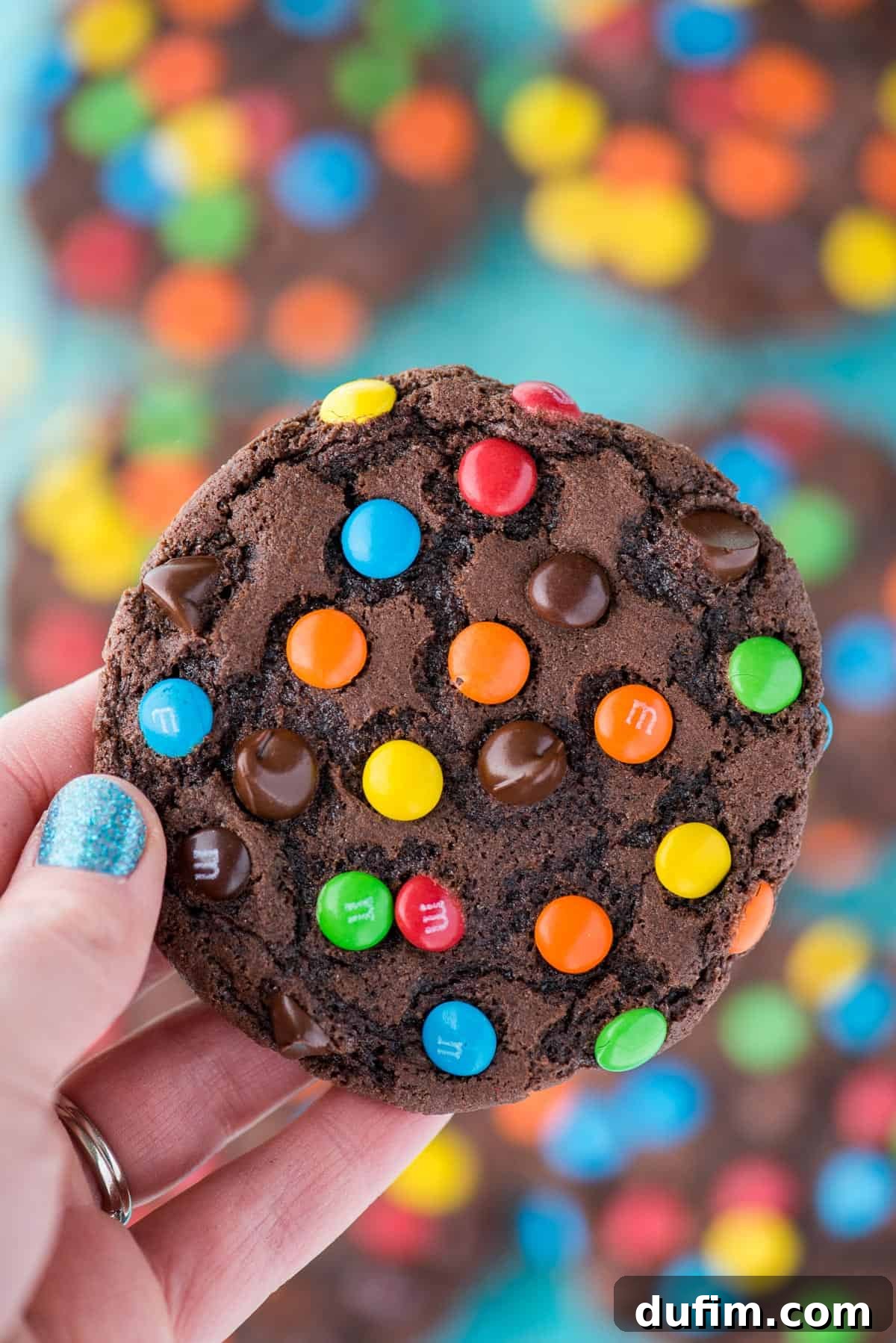 These double chocolate chip M&M cookies are easy to make, only 20 minutes from start to finish. Plus no chilling of the dough! These m&m cookies are chocolate-y, chewy & soft and loaded with m&m's and chocolate chips. #chocolatemmcookies #doublechocolatecookies #mmcookies hand holding double chocolate chip cookie with m&m's and chocolate chips