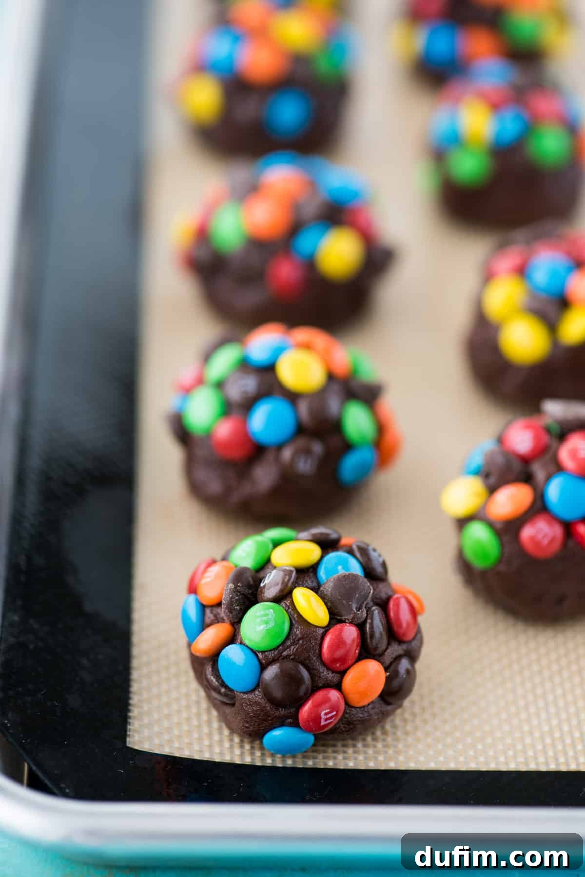 These double chocolate chip M&M cookies are easy to make, only 20 minutes from start to finish. Plus no chilling of the dough! These m&m cookies are chocolate-y, chewy & soft and loaded with m&m's and chocolate chips. #chocolatemmcookies #doublechocolatecookies #mmcookies double chocolate chip cookie dough balls with m&m's and chocolate chips on silicone baking mat