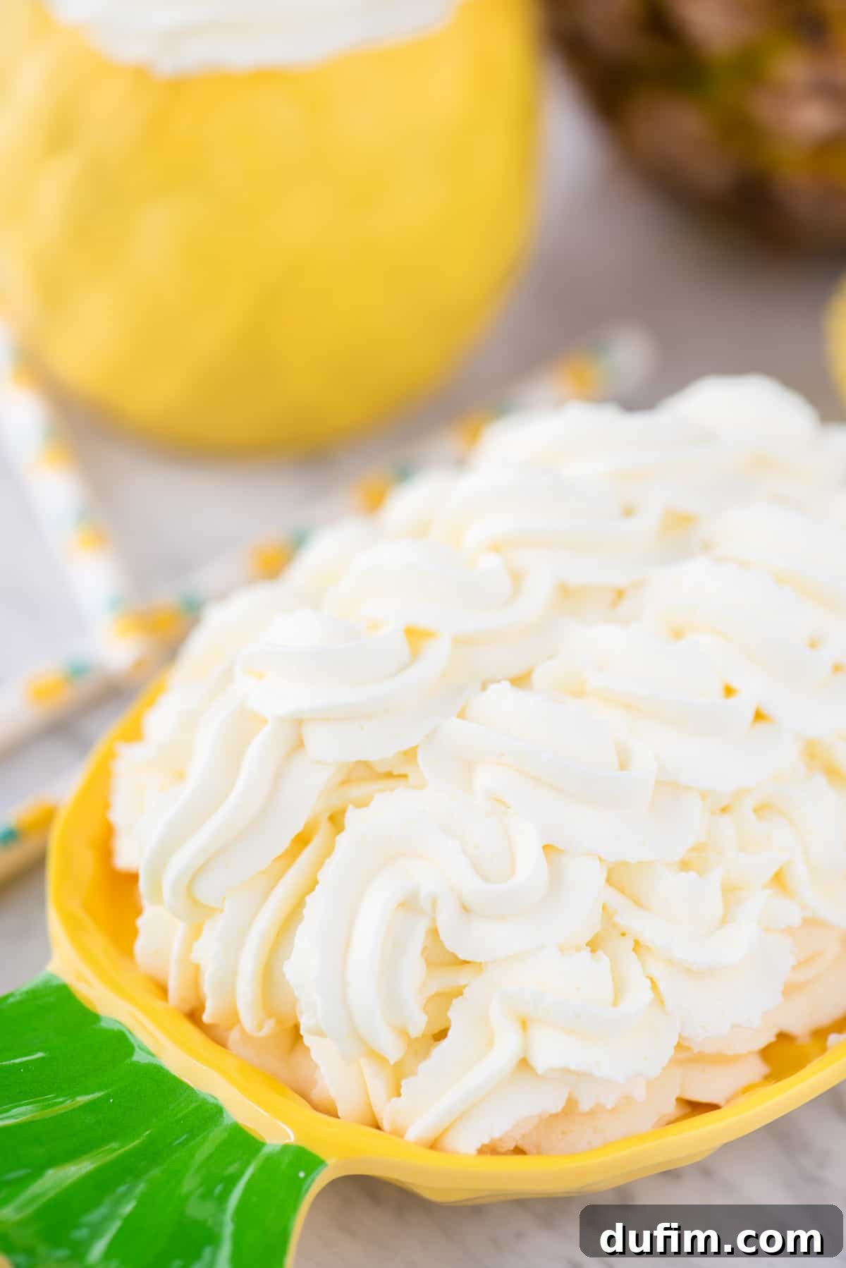 Fluffy pineapple whipped cream frosting meticulously piped onto a charming pineapple-shaped plate, showcasing its firm, yet airy texture. This presentation emphasizes its readiness as a delicious topping for various desserts.