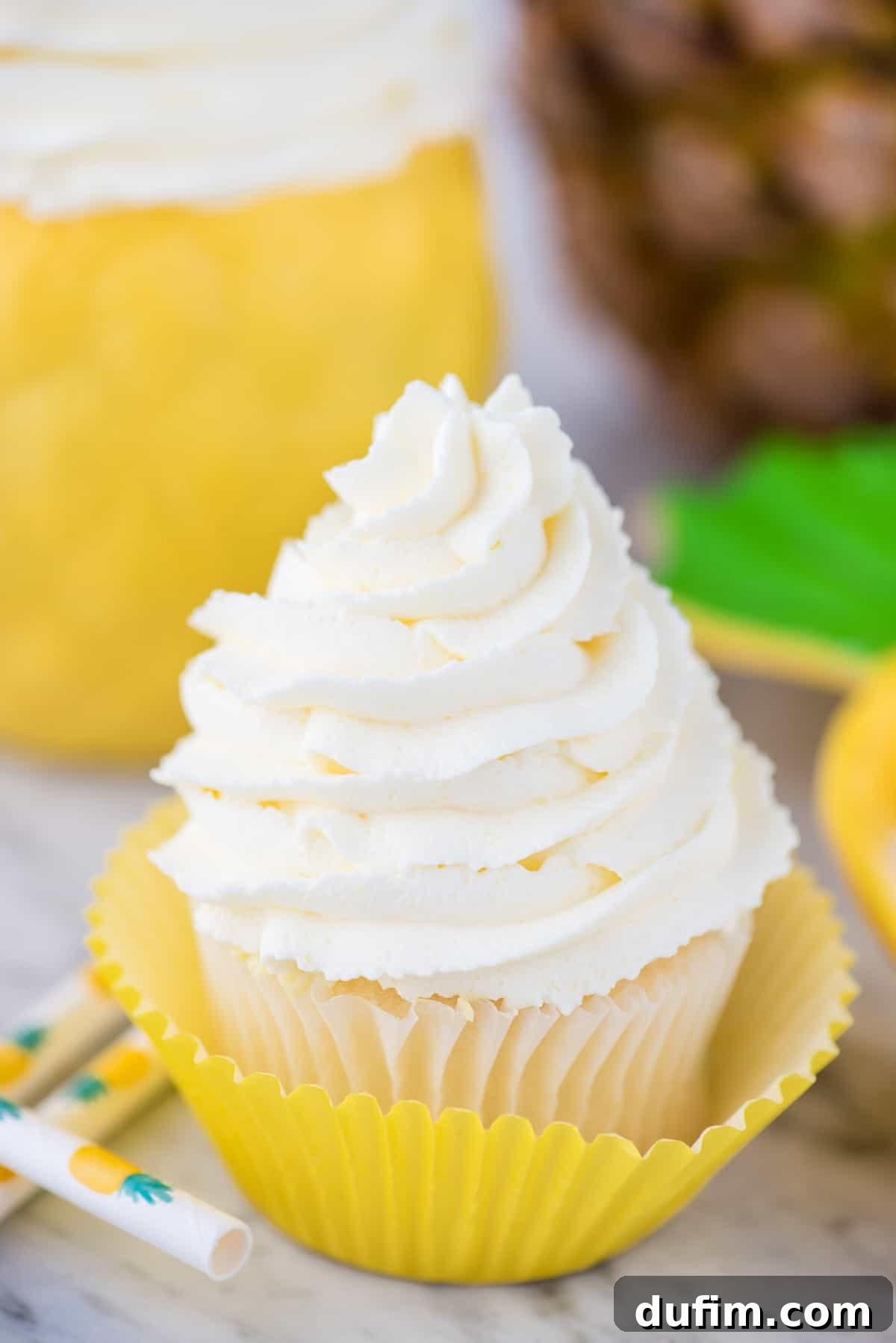 A perfectly frosted white cupcake adorned with a generous, artfully piped swirl of vibrant pineapple whipped cream frosting, illustrating its ideal texture and readiness for serving as a delightful dessert.