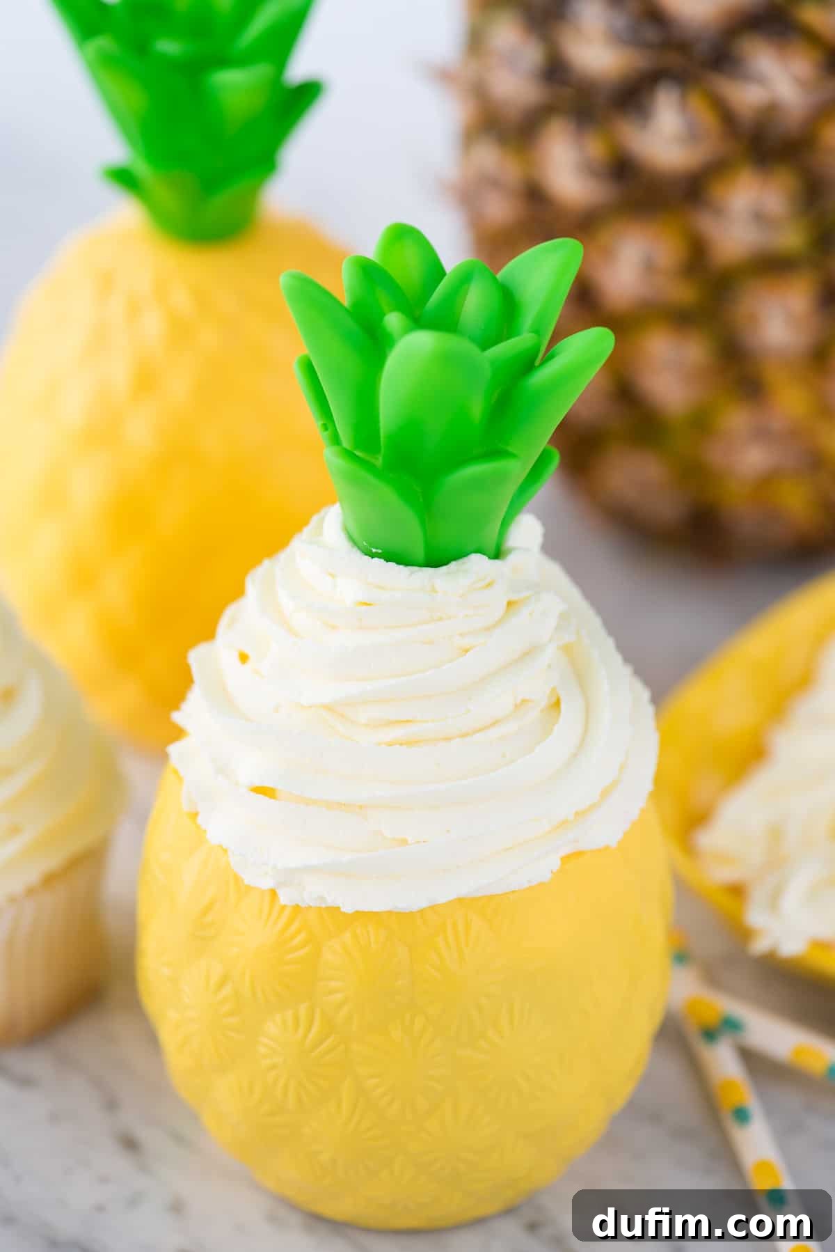 A close-up shot of creamy pineapple whipped cream frosting, beautifully piped inside a clear plastic pineapple-shaped cup, highlighting its smooth texture and individual serving potential for a refreshing dessert.