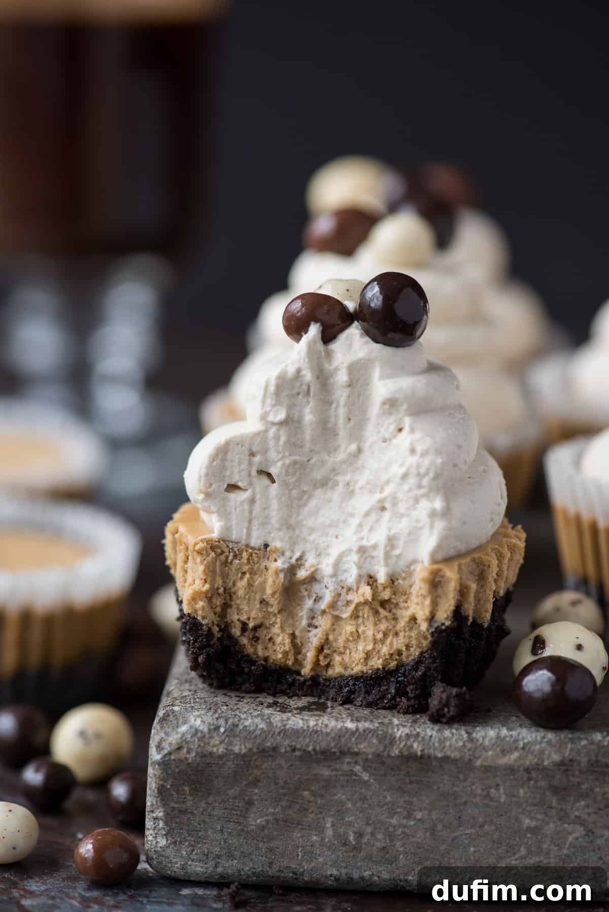 This is a crowd favorite mini coffee cheesecake recipe that you’ll use over and over! The whole recipe is only 7 ingredients and you make it in a regular size muffin pan! Plus, you can do an oreo crust or graham cracker crust for these mini espresso cheesecakes. #minicheesecake #coffeecheesecake #minicoffeecheesecake #espressocheesecake #mochacheesecake A close-up of a single mini coffee cheesecake on a rustic stone slab, topped with generous swirls of whipped cream and garnished with three dark chocolate-covered espresso beans, highlighting its elegant simplicity and inviting texture.