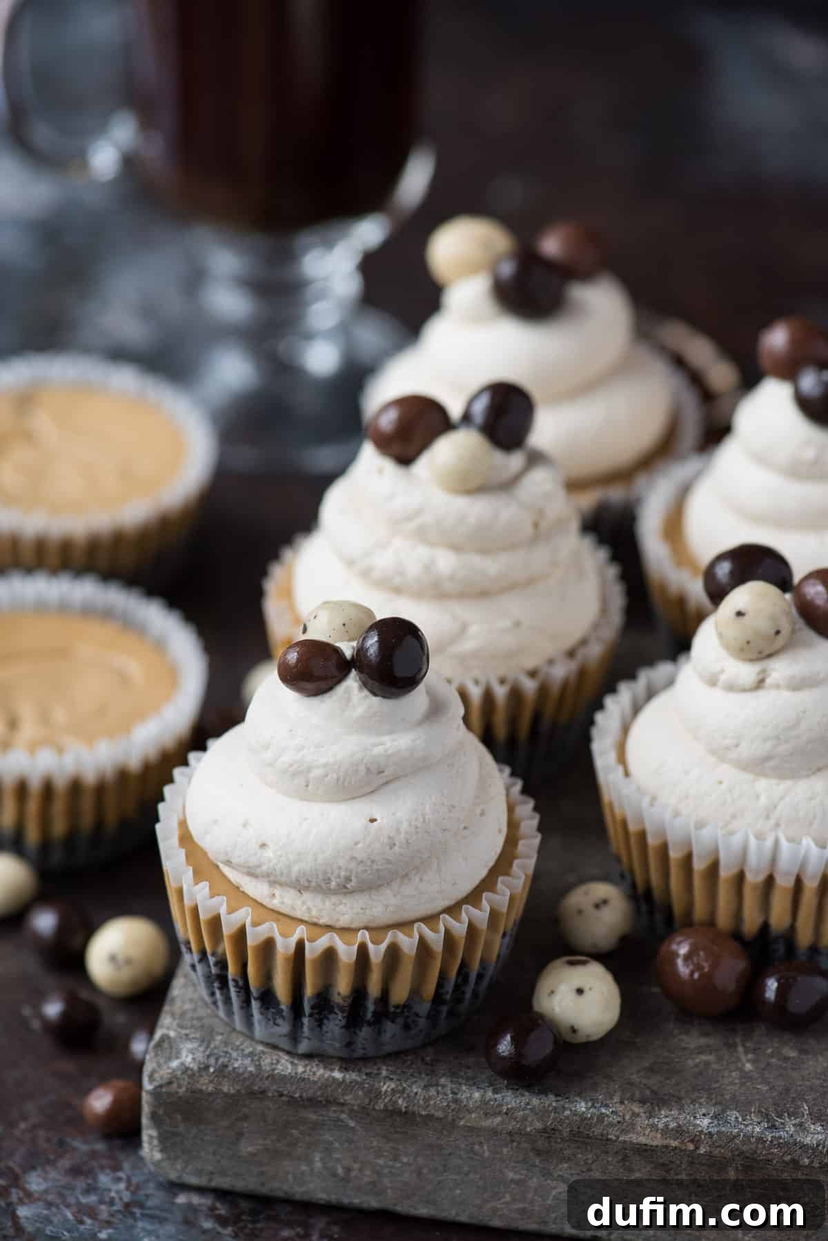 This is a crowd favorite mini coffee cheesecake recipe that you’ll use over and over! The whole recipe is only 7 ingredients and you make it in a regular size muffin pan! Plus, you can do an oreo crust or graham cracker crust for these mini espresso cheesecakes. #minicheesecake #coffeecheesecake #minicoffeecheesecake #espressocheesecake #mochacheesecake Multiple mini coffee cheesecakes artfully arranged on a stone slab, each topped with a delicate swirl of whipped cream and a few dark espresso beans, inviting guests to indulge in their rich flavor.