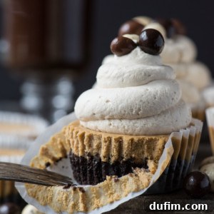 A close-up of a cupcake with a chocolate base, graham cracker crust, and swirled frosting topped with chocolate-covered balls. The partially peeled wrapper and fork evoke the look of mini coffee cheesecakes, with more treats and a drink in the background.