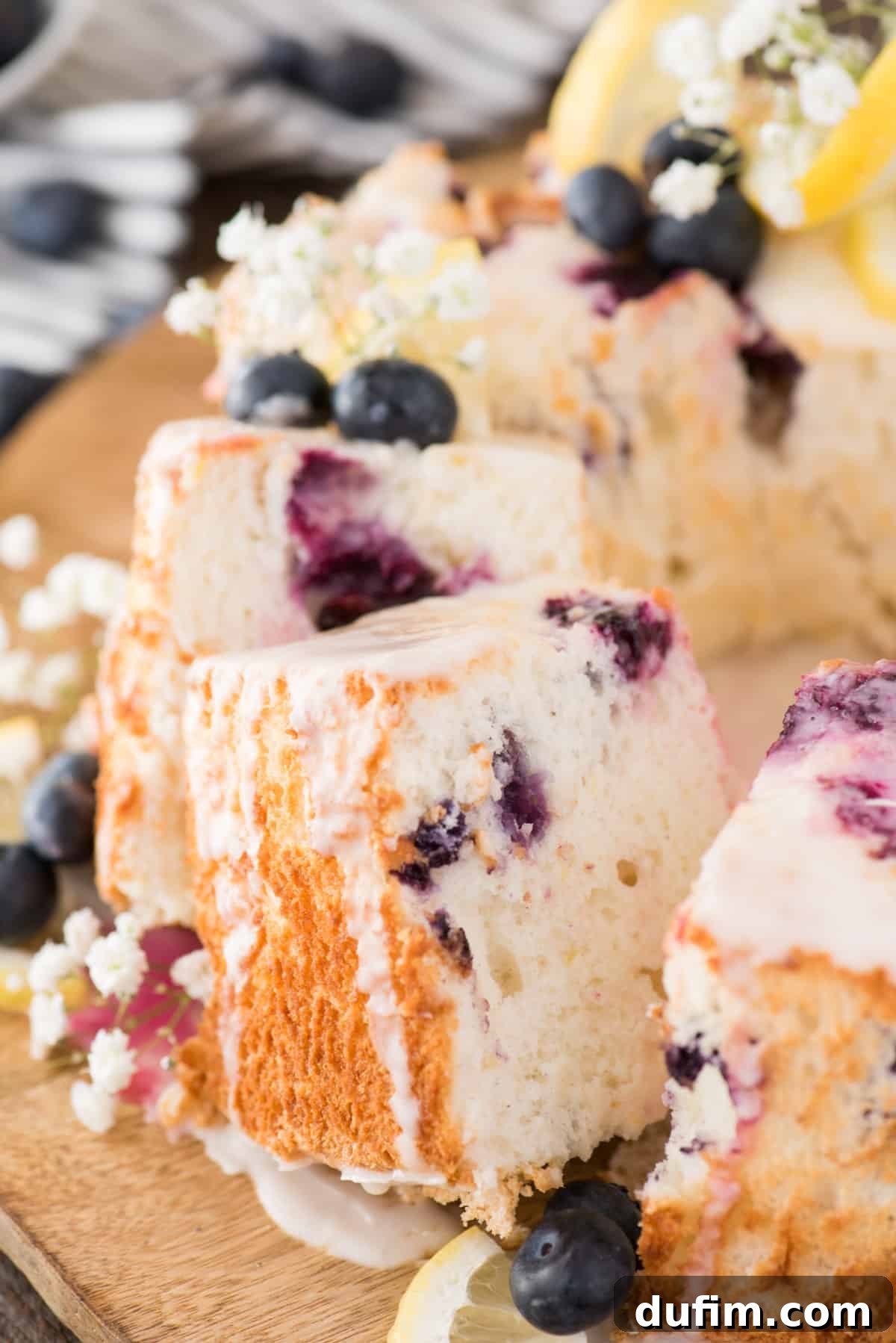 Beautifully sliced lemon blueberry angel food cake on a wooden plate, showcasing its fluffy texture and the embedded blueberries.