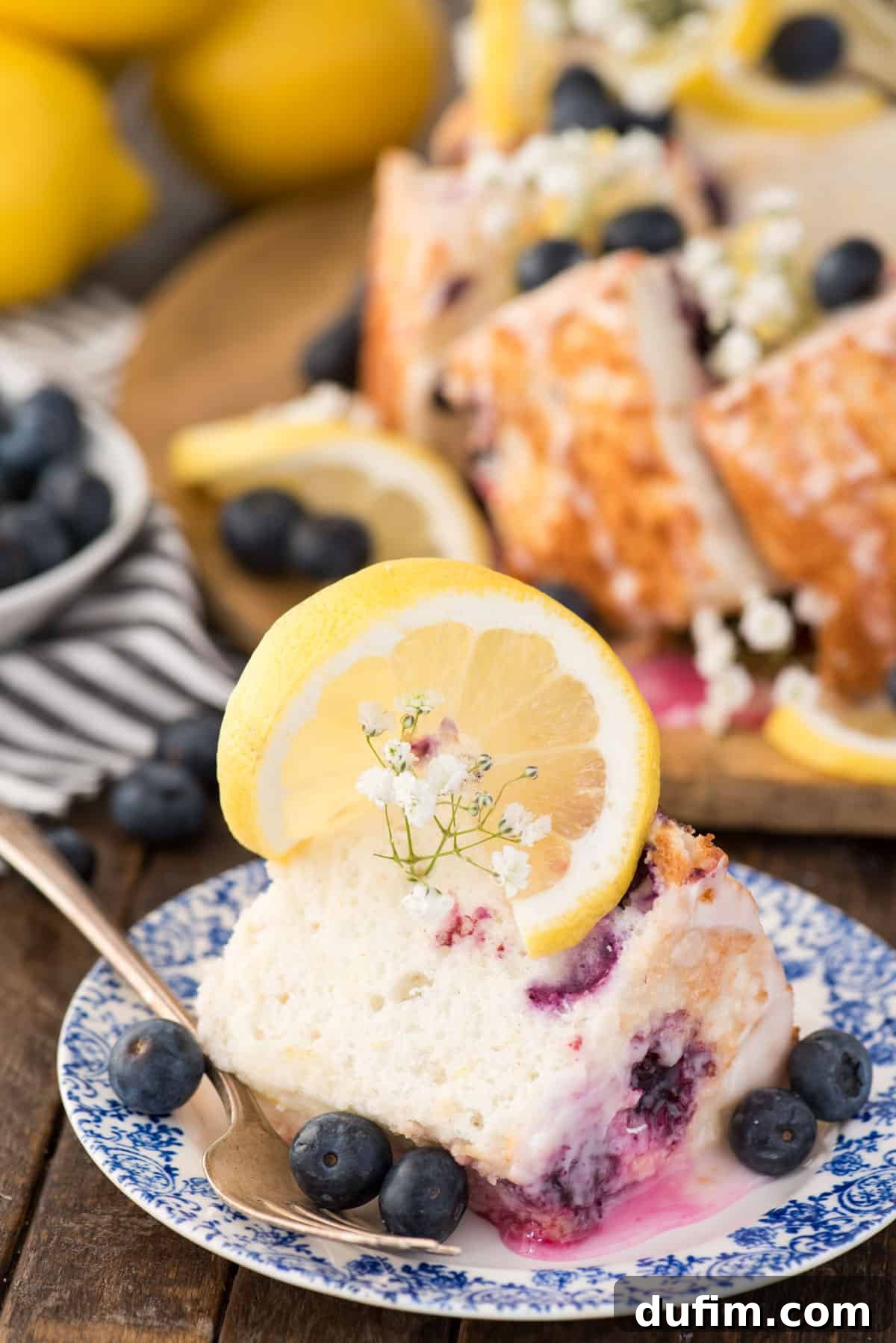 A single slice of lemon blueberry angel food cake artfully placed on a blue and white floral plate, against a warm wooden background.