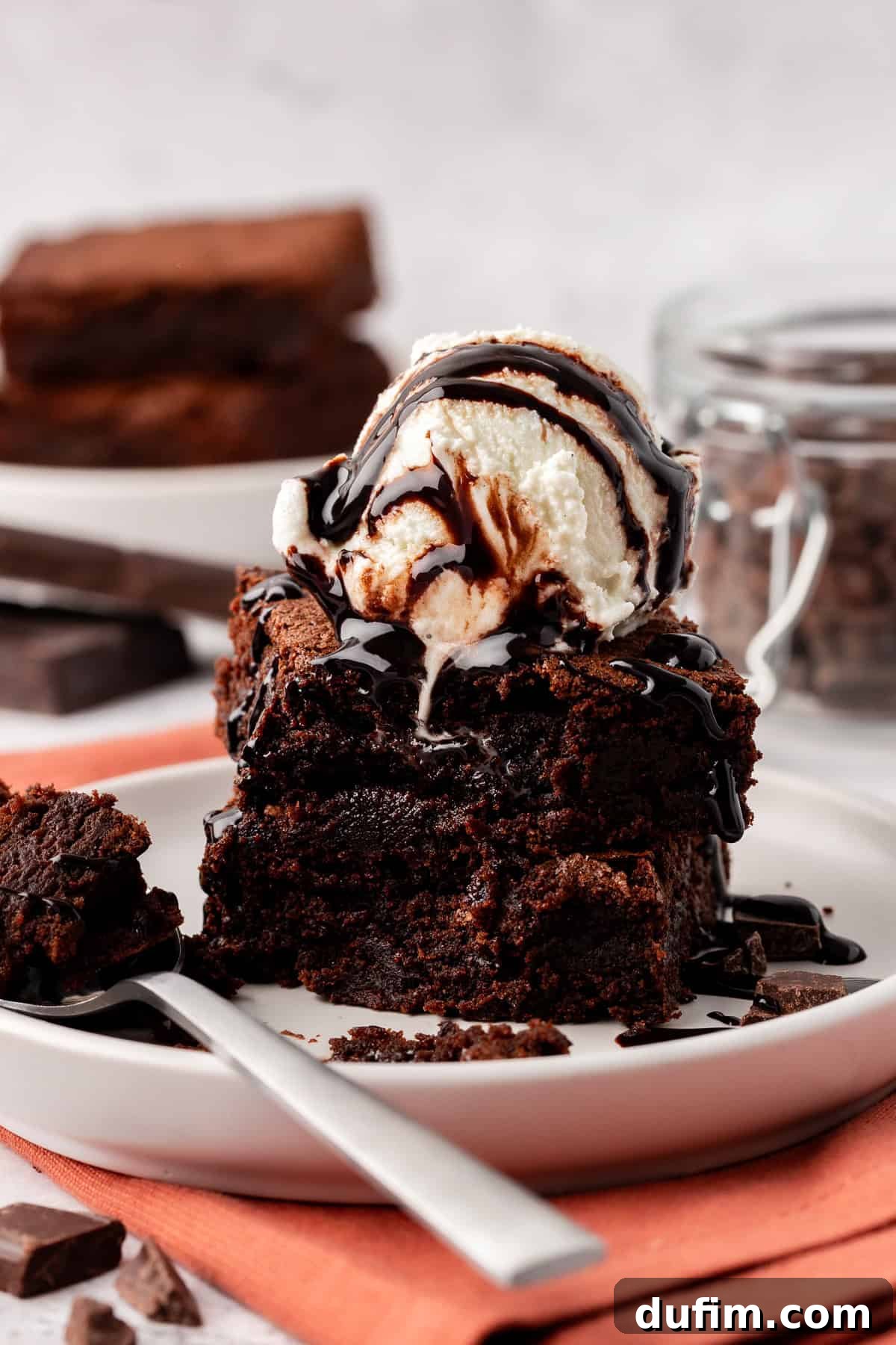 Decadent Chocolate Brownies 2 Two rich, fudgy homemade brownies stacked, topped with creamy vanilla ice cream, against a clean white background, highlighting their perfect texture and shiny crust.