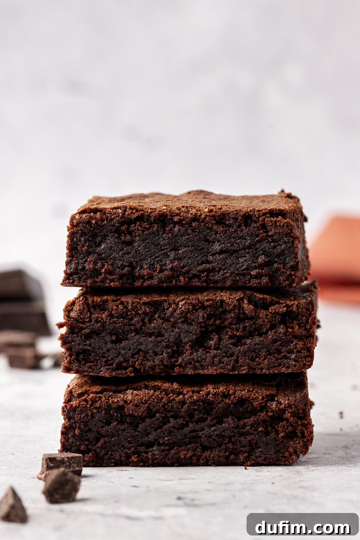 Decadent Chocolate Brownies 18 Three perfectly baked classic homemade brownies stacked, showcasing their incredible height, dense texture, and signature shiny, crinkly tops.
