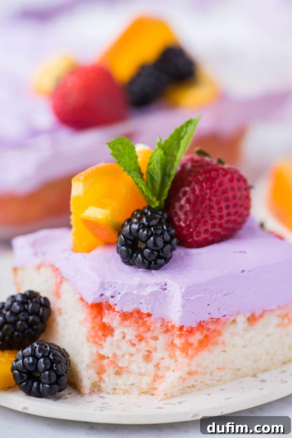 A single slice of Sangria Poke Cake, elegantly presented on a white plate, adorned with a fresh strawberry, a few blackberries, a vibrant orange slice, and a delicate mint leaf, highlighting its irresistible appeal.
