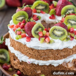 strawberry angel food cake topped with whipped cream, whole strawberries, chopped strawberries and kiwi on wooden serving tray