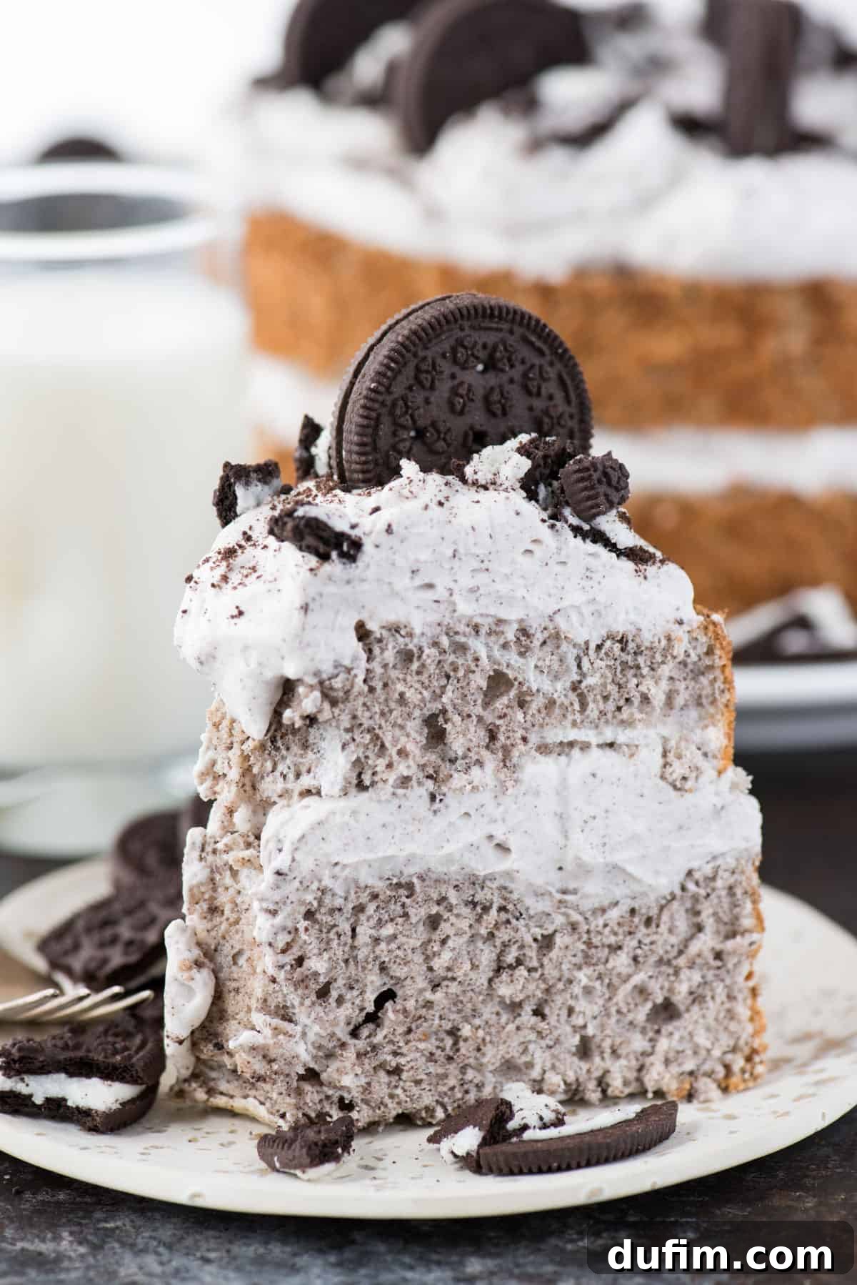 Slice of Oreo Angel Food Cake with Oreo whipped cream and crushed Oreo pieces on a white plate on a dark background