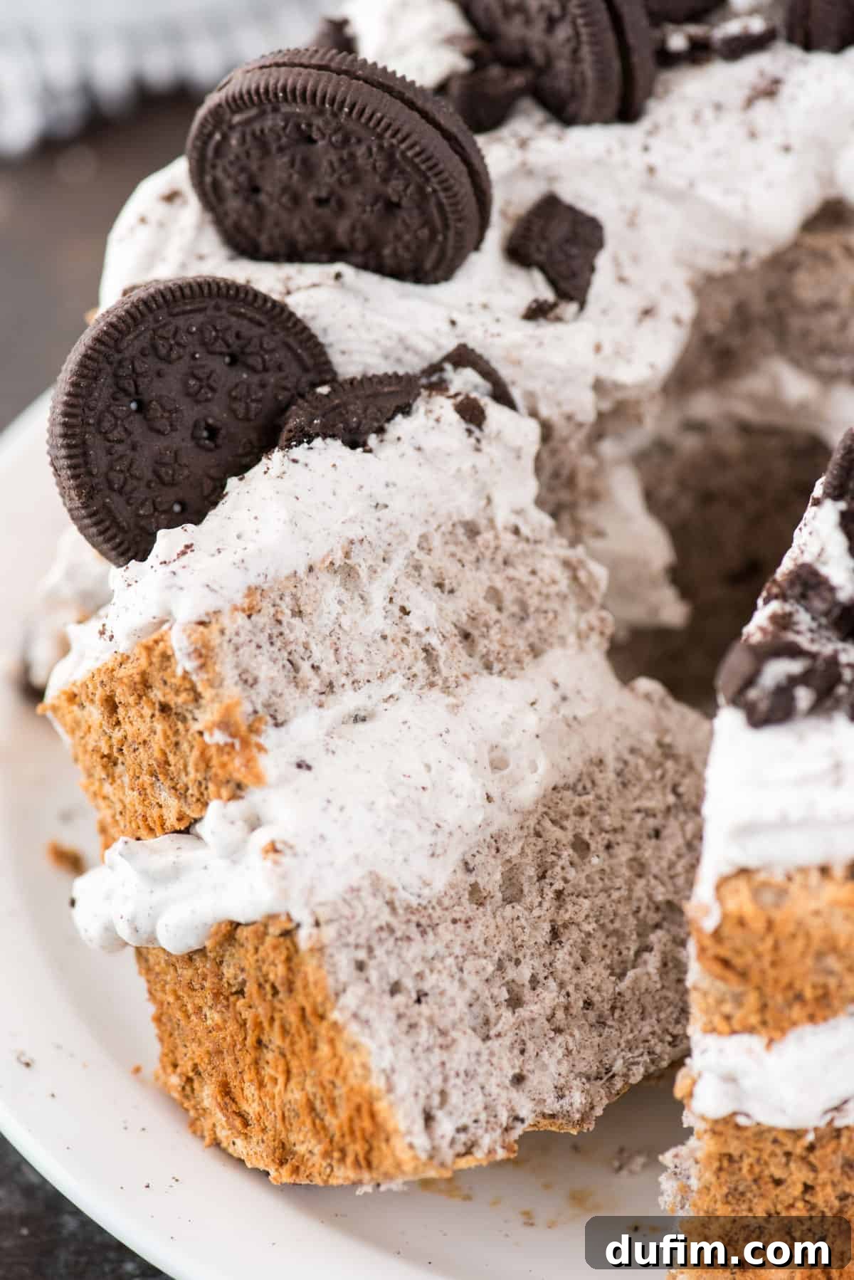 Slice of Oreo Angel Food Cake with Oreo whipped cream and crushed Oreo pieces on a white plate on a dark background