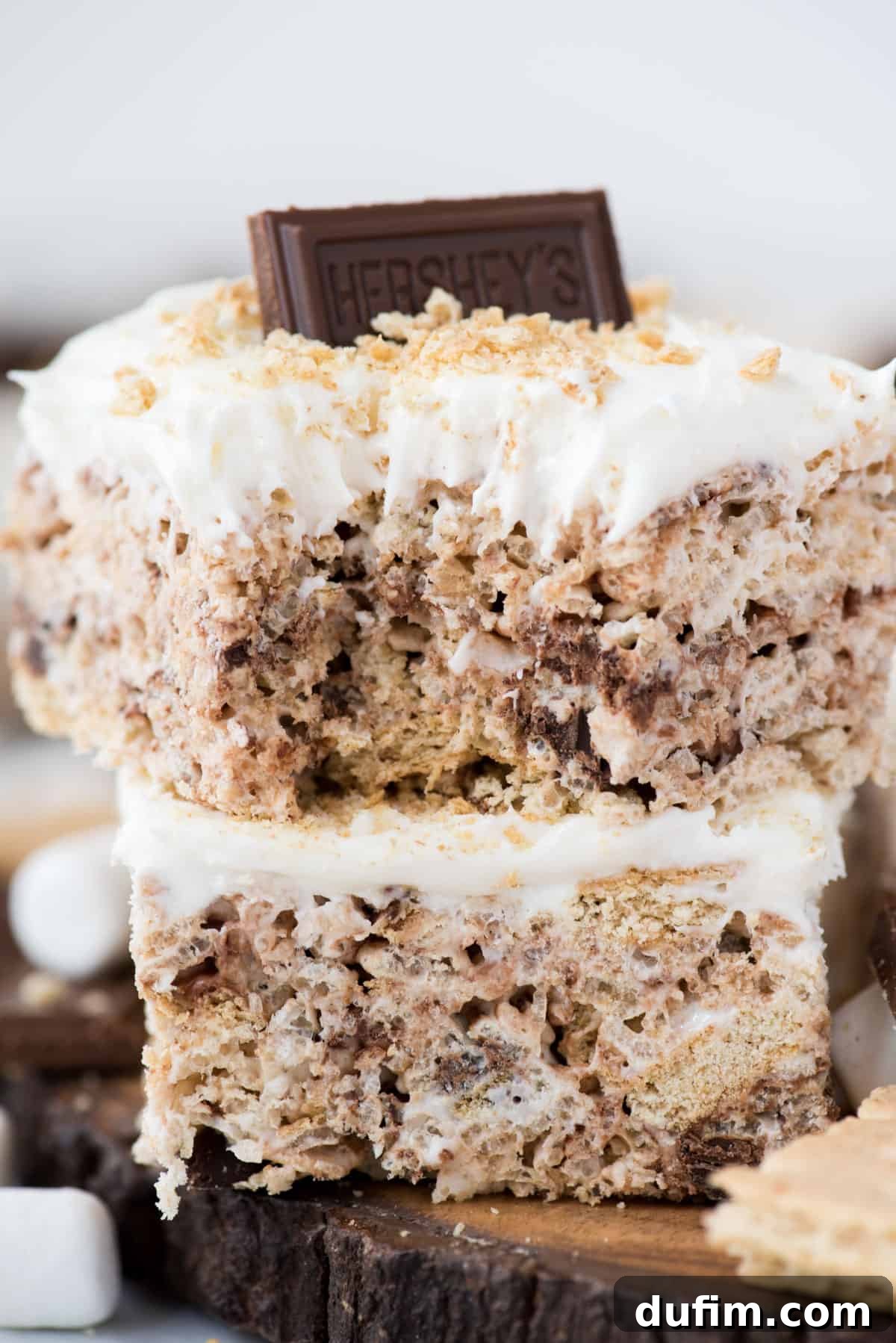 No-Bake S'mores Rice Krispie Treats 2 Two s’mores rice krispie treats cut into squares and stacked on top of each other close up, showcasing gooey marshmallow frosting and chocolate pieces.