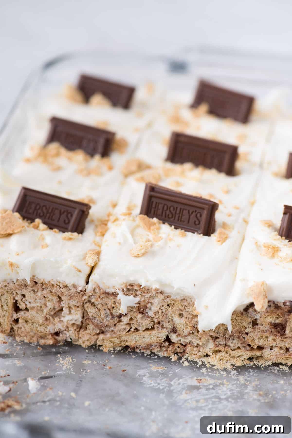 No-Bake S'mores Rice Krispie Treats 6 A vibrant close-up of S'mores bars topped with a luscious marshmallow frosting and adorned with classic Hershey's chocolate bars, nestled in a glass 9x13 inch pan.