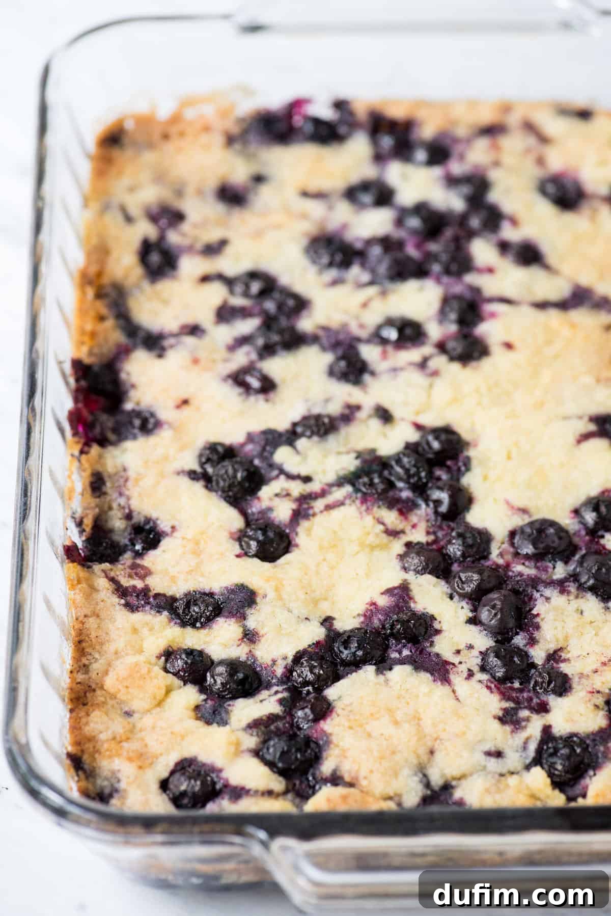 Zesty Lemon Blueberry Bake 3 Close-up shot of a golden-brown Lemon Blueberry Dump Cake cooling in a glass 9x13 inch baking pan, ready to be served.