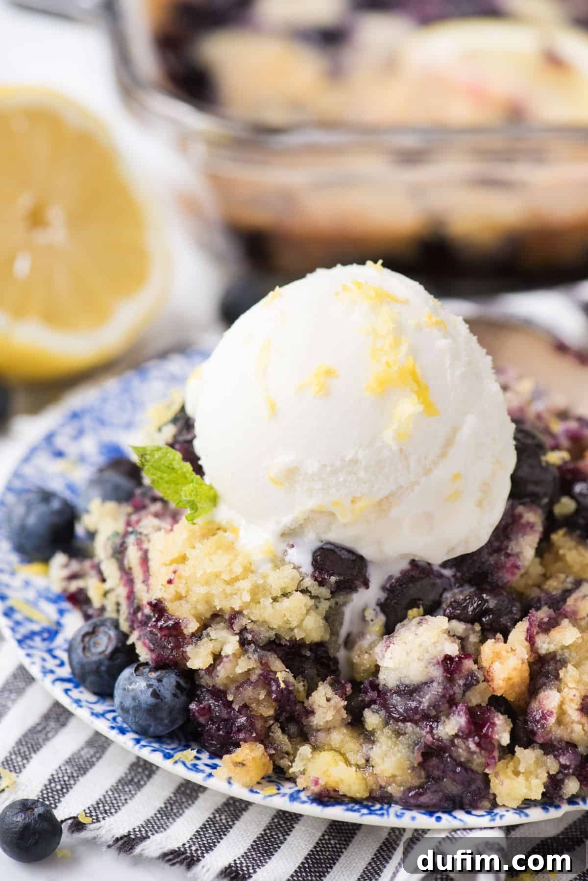 Zesty Lemon Blueberry Bake 6 A tempting scoop of Lemon Blueberry Dump Cake served on a blue floral plate, topped with a generous scoop of vanilla ice cream, ready to be enjoyed.