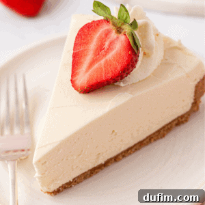 Whip Up a Philadelphia No Bake Cheesecake 17 A slice of creamy Philadelphia No-Bake Cheesecake with a crumbly crust, topped with whipped cream and a halved strawberry, served on a white plate with a fork beside it.