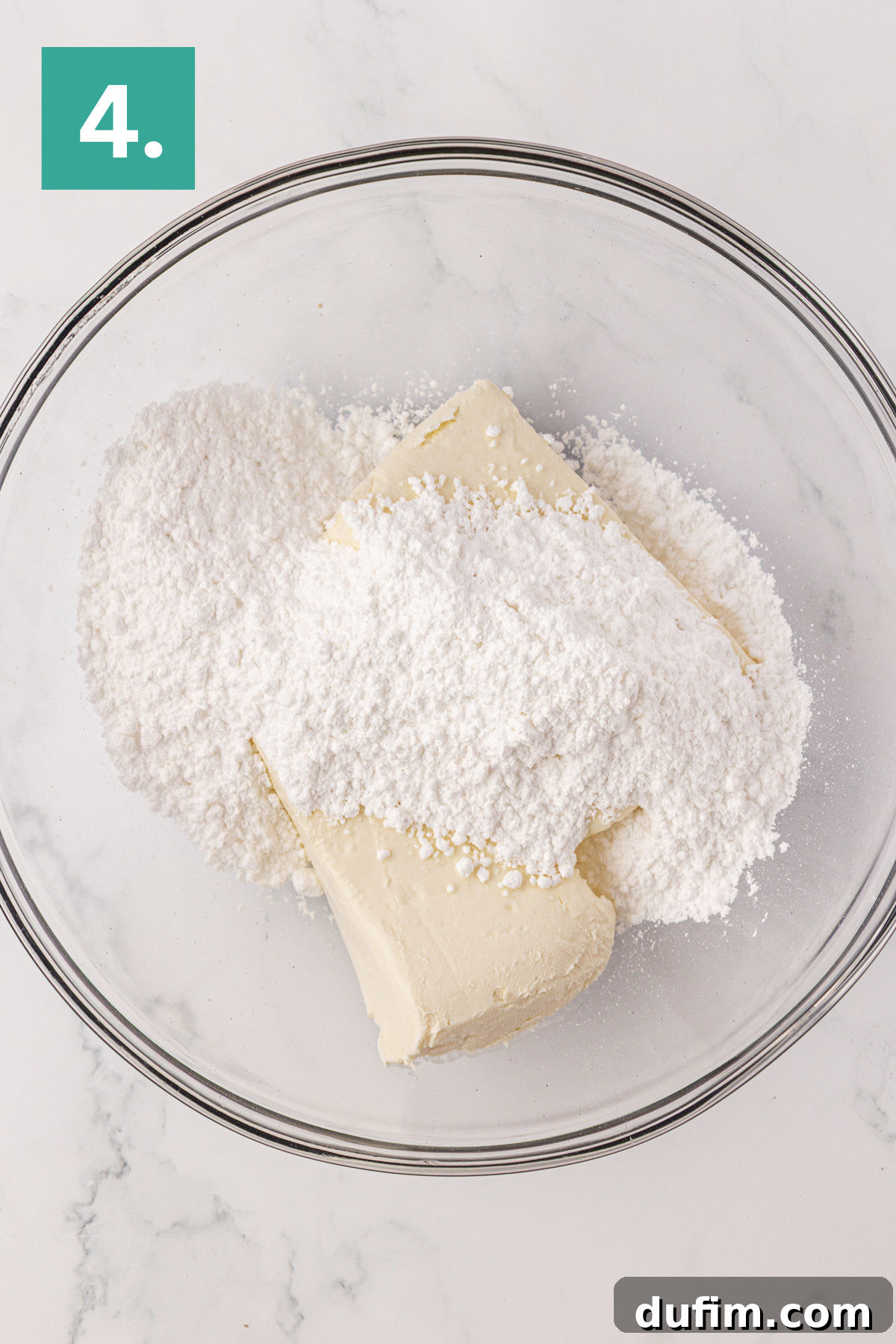 Whip Up a Philadelphia No Bake Cheesecake 9 A transparent glass mixing bowl containing softened cream cheese and a generous amount of powdered sugar, perfectly prepped for crafting a luscious Philadelphia no-bake cheesecake. The bowl sits on a pristine white surface, prominently marked with a green square displaying the number '4' in white in the top-left corner, signifying the next step in the preparation.