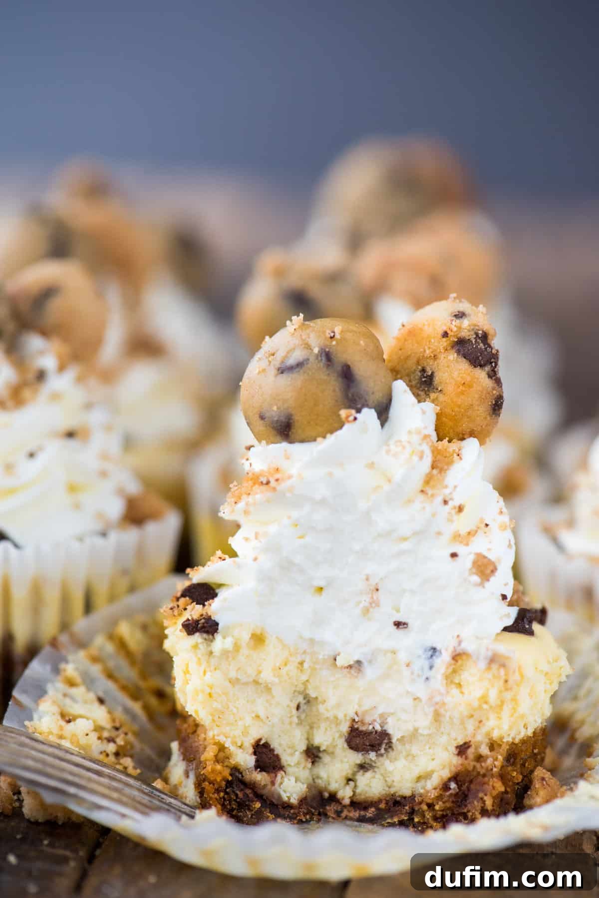 A mini chocolate chip cookie dough cheesecake with a bite removed, showcasing its layers of cookie crust and creamy filling, set on a textured wooden background.