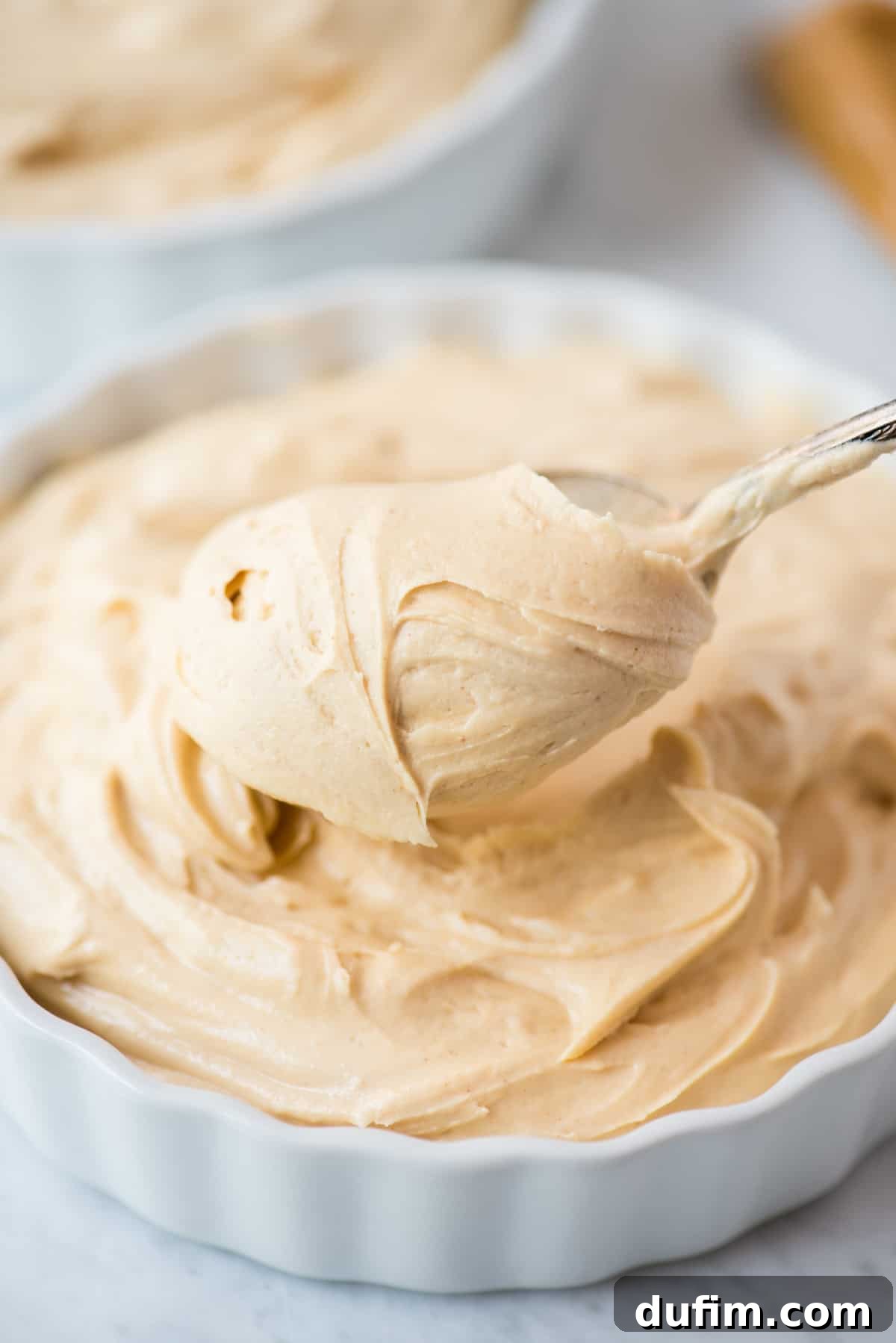 Decadent Peanut Butter Fluff 2 A close-up of rich, creamy peanut butter frosting in a pristine white bowl, with a spoon perfectly poised, inviting you to indulge.