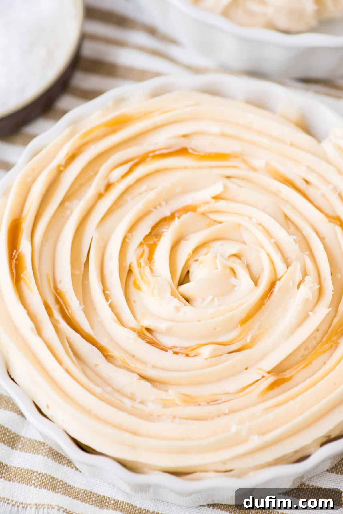 Salted Caramel Buttercream Perfection 5 A close-up view of delectable salted caramel frosting in a white bowl, with rich caramel sauce elegantly swirled throughout, ready to be spread or piped onto your favorite desserts.