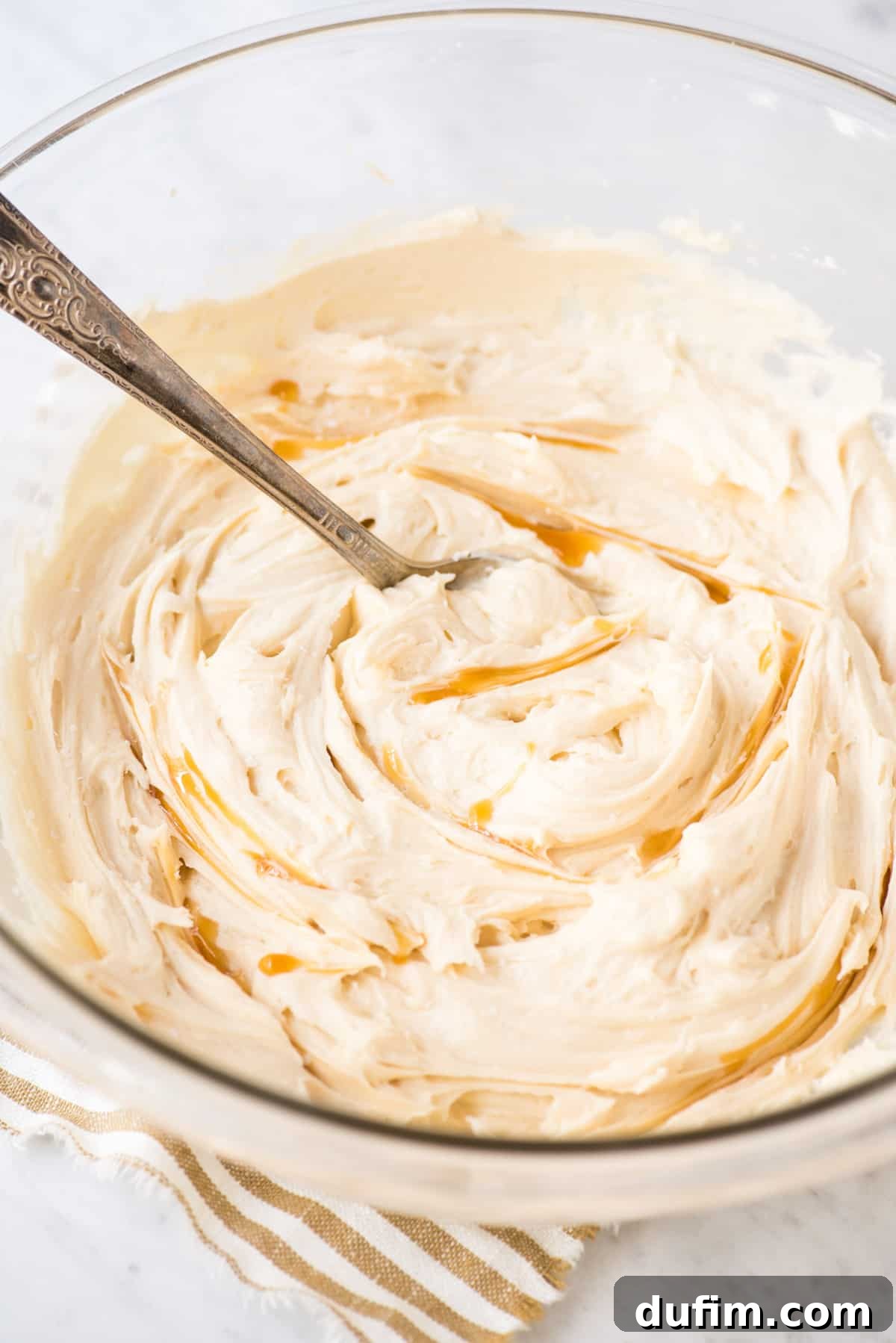 Salted Caramel Buttercream Perfection 6 A close-up of smooth, luscious salted caramel frosting with streaks of caramel sauce swirled beautifully within, presented in an elegant glass bowl, ready for frosting baked goods.