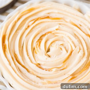 A close-up of a dish filled with creamy, whipped butter swirled in a spiral pattern, reminiscent of salted caramel frosting, drizzled with honey, and sprinkled with sea salt. The dish sits on a striped cloth.
