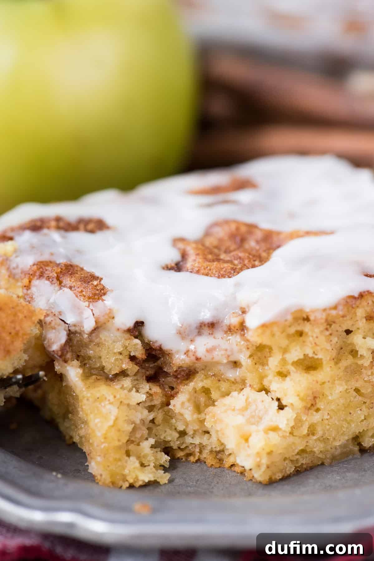 Effortless Apple Spice Coffee Cake 12 A perfectly sliced piece of apple coffee cake, topped with sweet white icing, presented on a metal plate with a fresh green apple in the background.