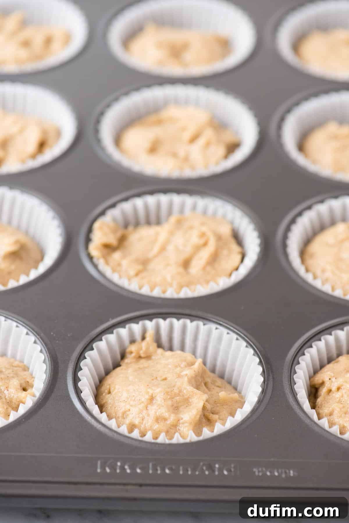 Spiced Apple Harvest Cupcakes 4 Close-up view of apple spice cupcake batter expertly portioned into a metal muffin pan, ready for baking.