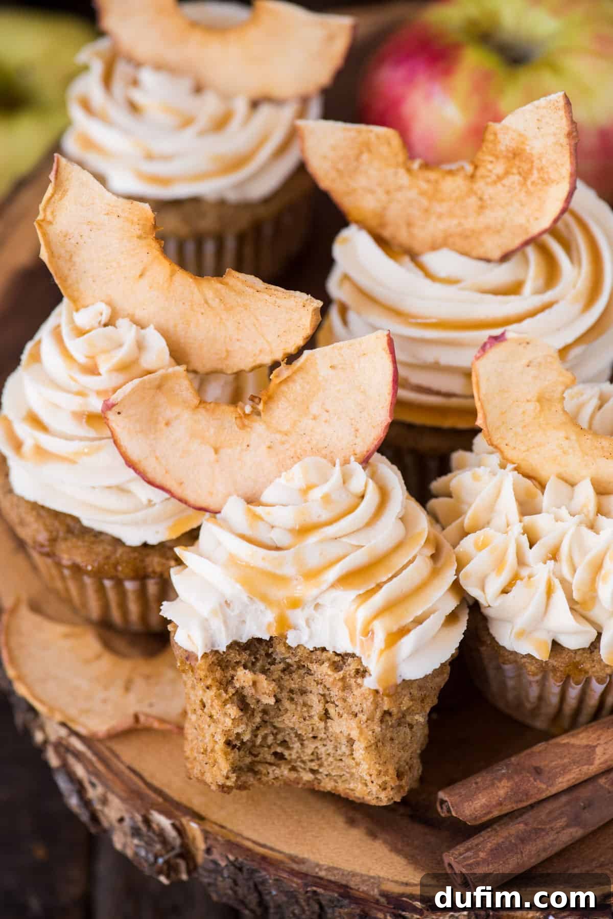 Spiced Apple Harvest Cupcakes 6 A vibrant display of apple spice cupcakes with generous swirls of salted caramel frosting and delicate apple chips, arranged beautifully on a rustic wooden cake stand.
