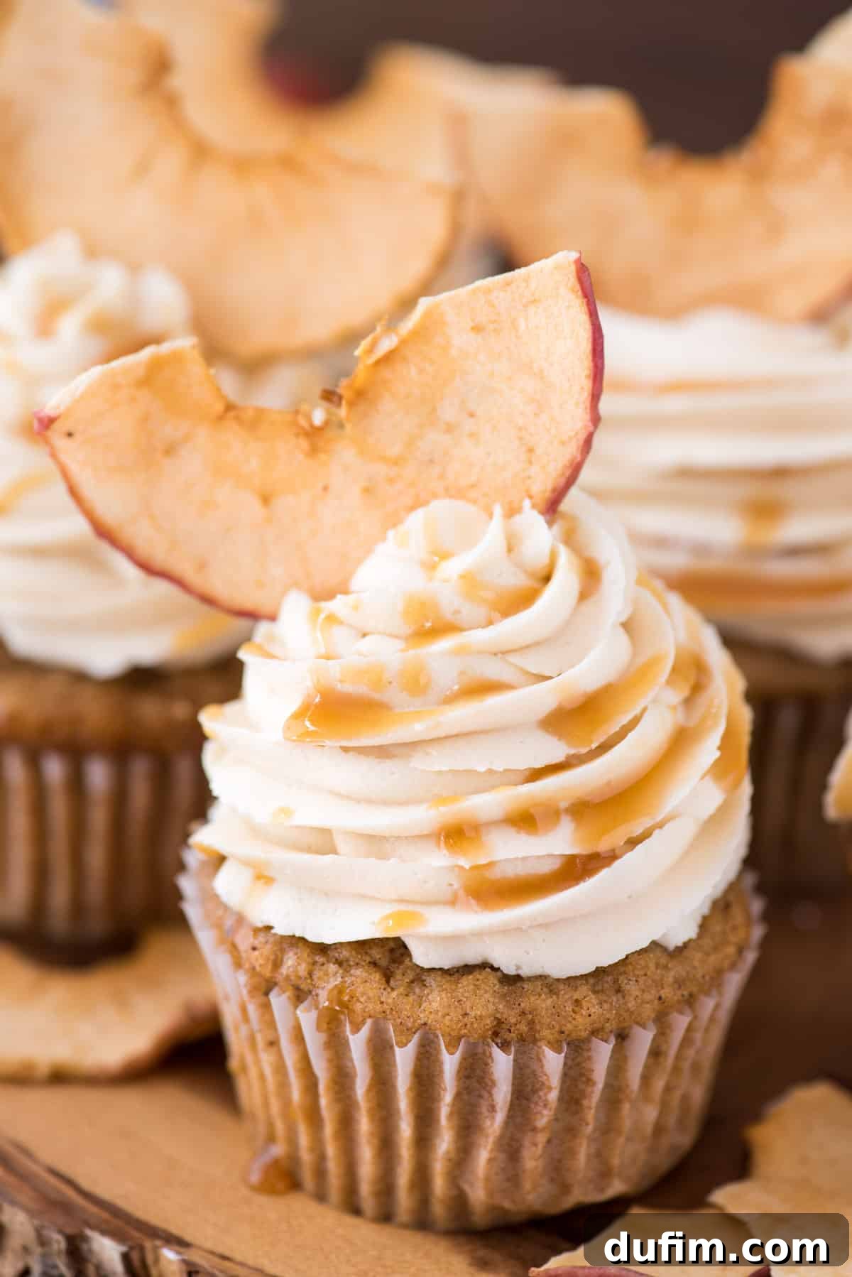 Spiced Apple Harvest Cupcakes 7 An inviting arrangement of apple spice cupcakes featuring salted caramel frosting and apple chips, elegantly displayed on a wooden cake stand, ready to be enjoyed.