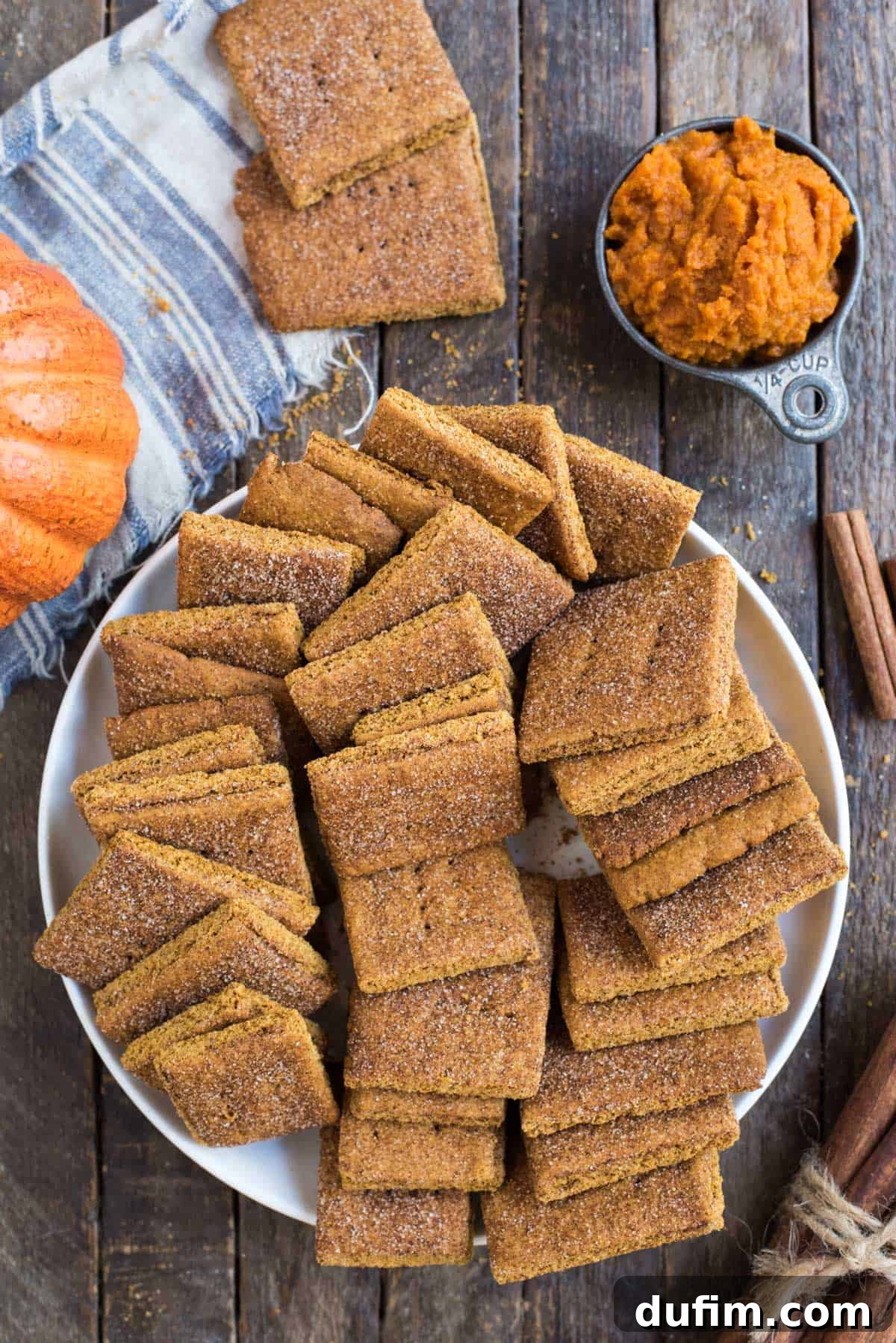 Pumpkin Spice Graham Snaps 3 A close-up shot of a stack of golden-brown pumpkin graham crackers in a white ceramic bowl, resting on a rustic wooden surface, highlighting their inviting texture and color.
