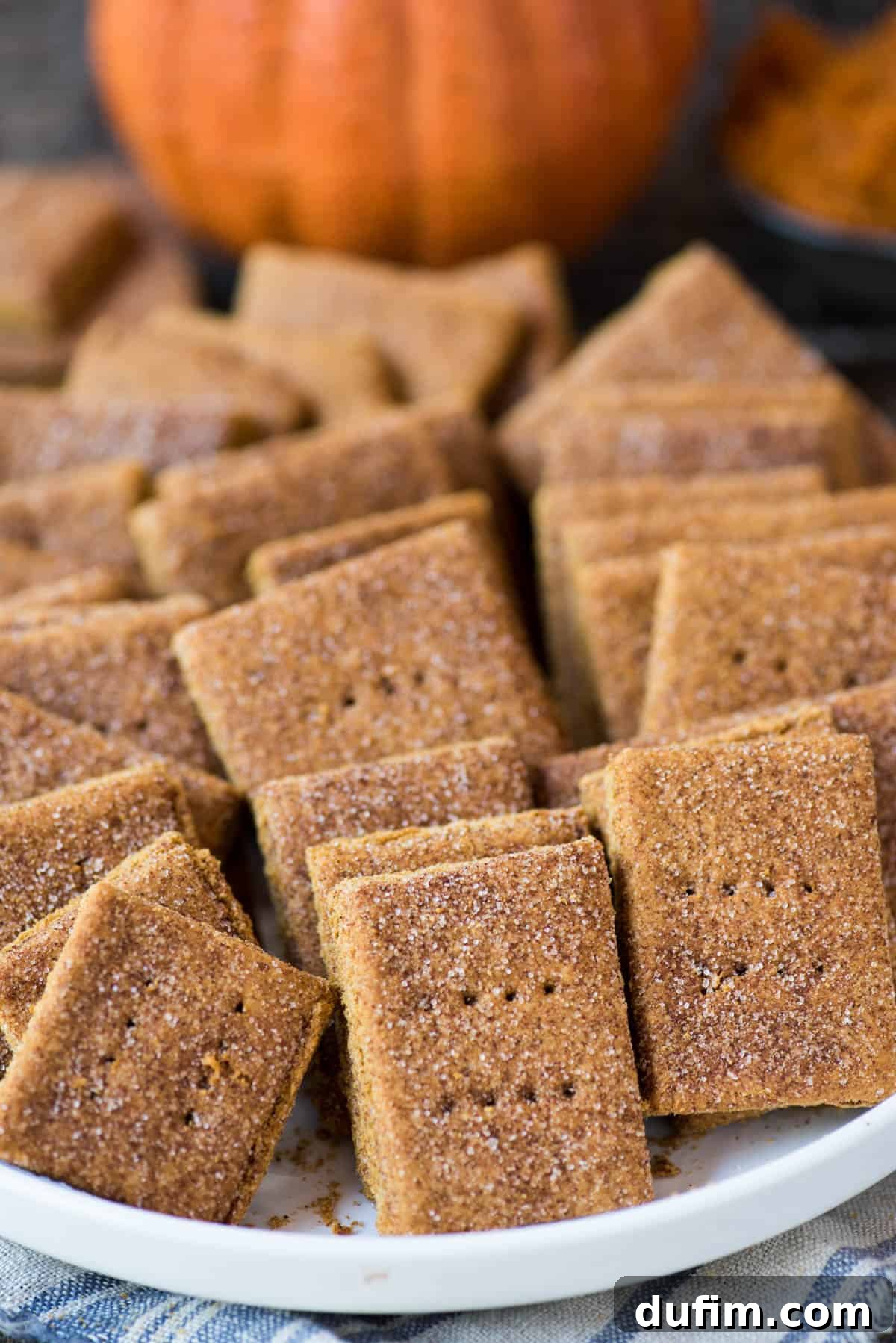 Pumpkin Spice Graham Snaps 6 A white bowl filled with freshly baked pumpkin graham crackers sits on a wooden background, showcasing the inviting golden hue and cinnamon sugar topping of the crackers.