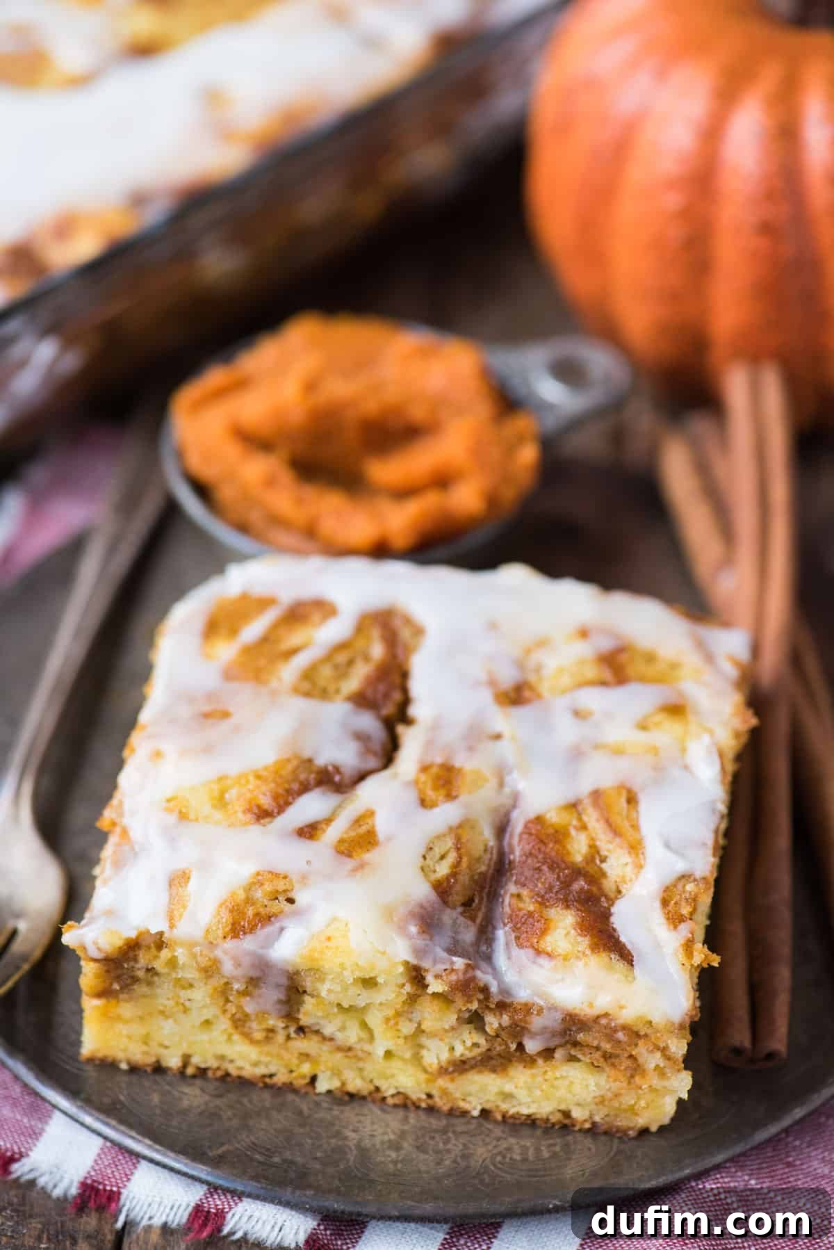 A tempting slice of easy pumpkin swirl cake, generously drizzled with a sweet white icing, presented beautifully on a metal plate. The swirled layers are visible, promising a burst of fall flavor.