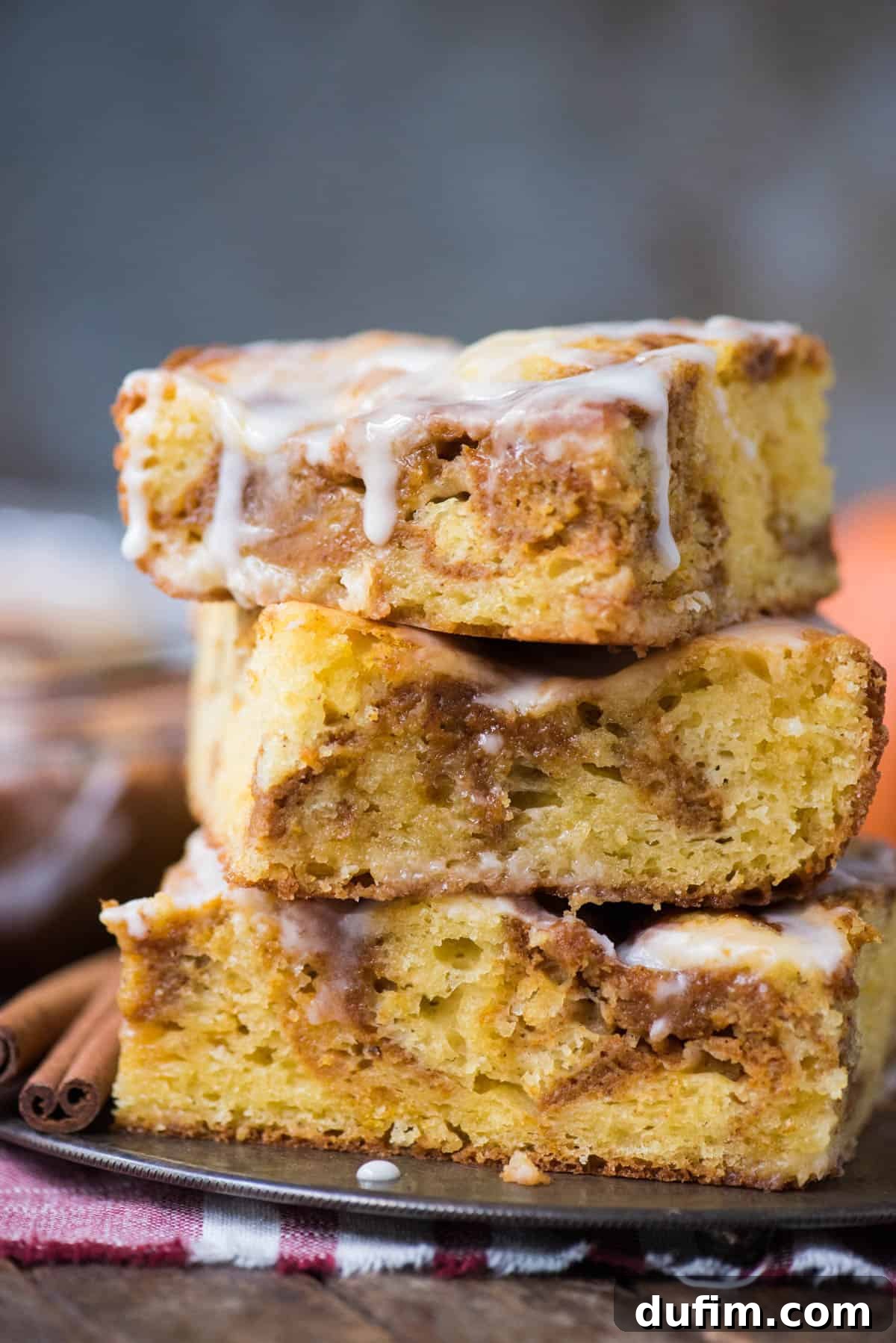 Three generous pieces of pumpkin coffee cake, expertly stacked on a rustic metal plate, showcasing the distinct yellow and pumpkin swirled layers and glistening white icing.