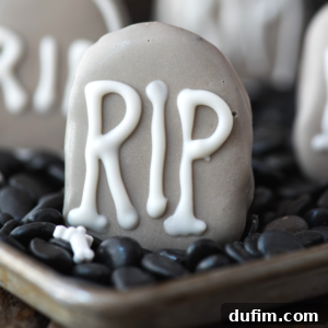 A gray tombstone-shaped cookie with 'RIP' in white icing, surrounded by black candy stones and other Halloween-themed Oreo balls.