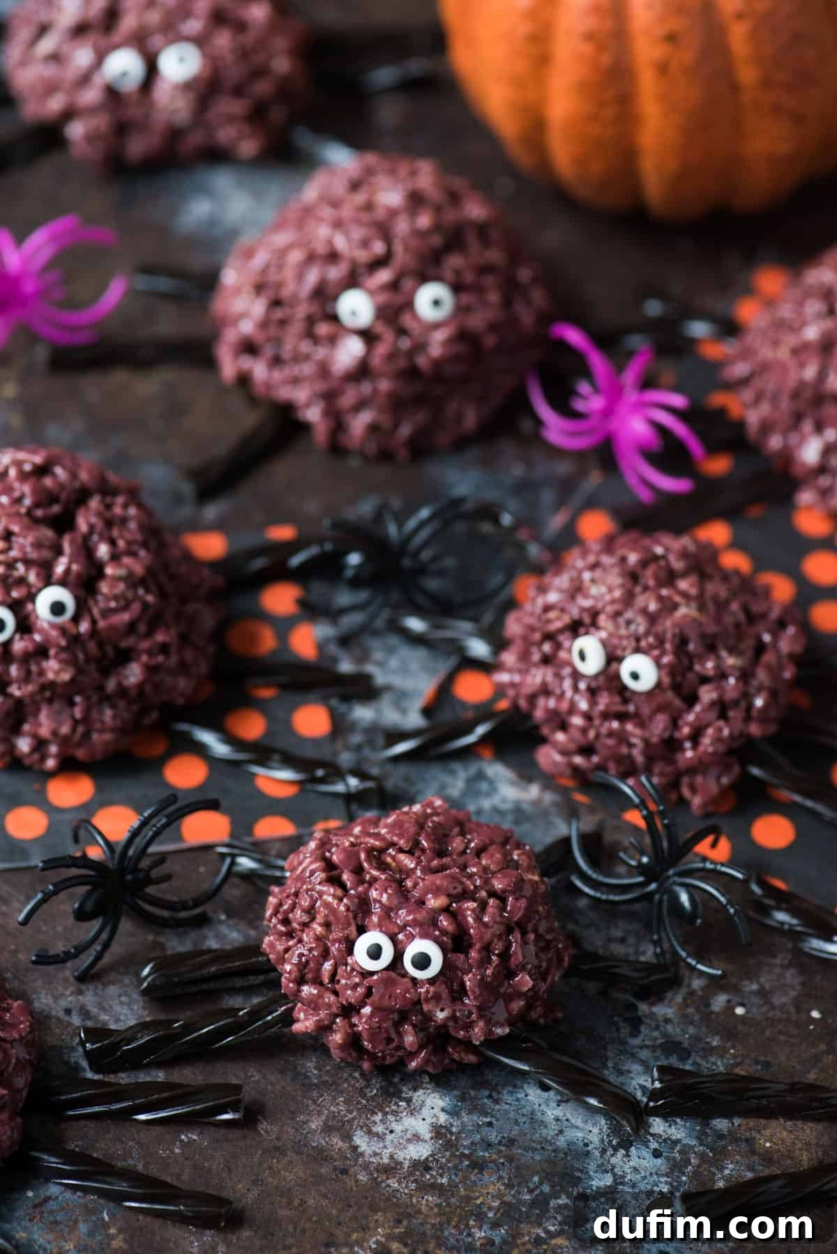 Spooky Spider Rice Krispie Treats 5 A close-up photograph of finished purple spider rice krispie treats, complete with black licorice legs and candy eyes, artfully displayed against a dark, moody background for Halloween.
