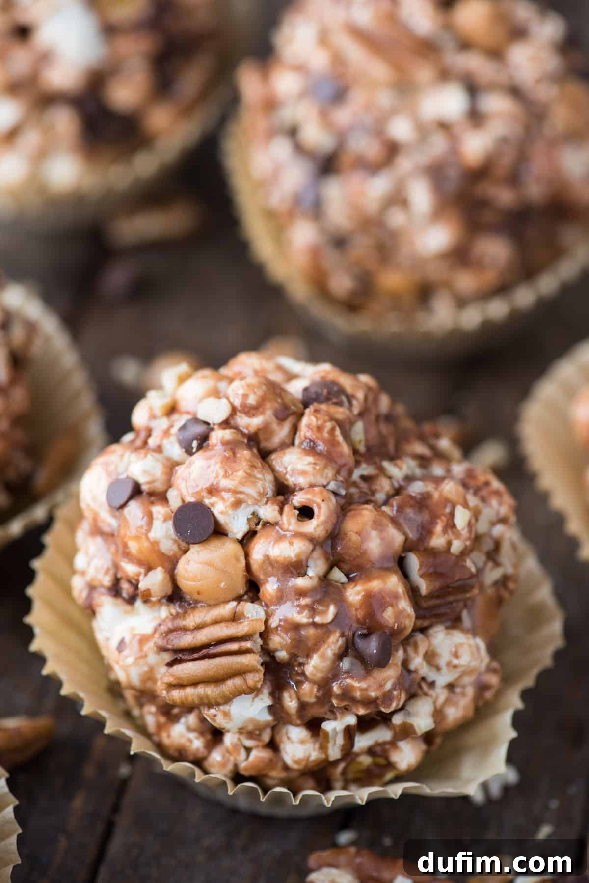 Turtle popcorn balls with caramel, chocolate, and pecans, beautifully presented in paper liners on a dark wooden background. Perfect for a holiday treat.