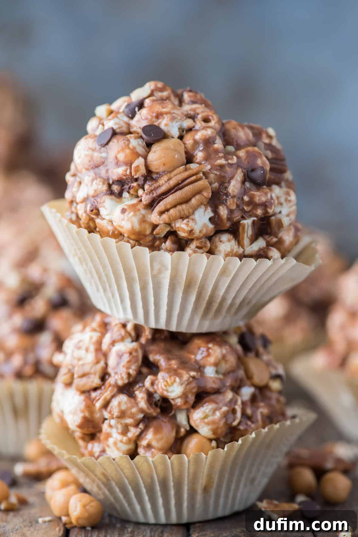 Two soft and chewy turtle popcorn balls, generously coated with caramel, chocolate, and pecans, stacked delicately on top of each other, showcasing their inviting texture.